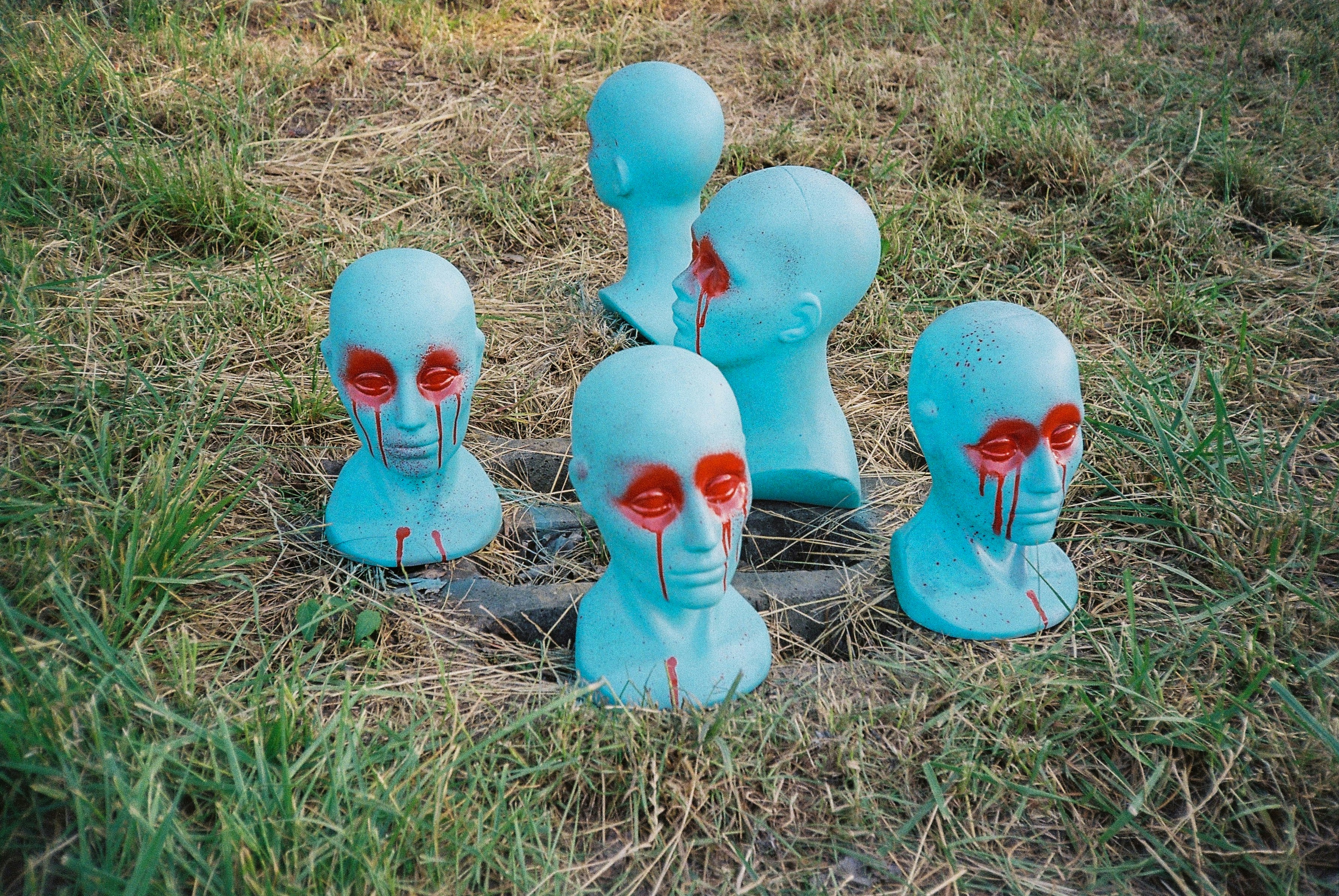 Blue mannequin heads with red eyes stand in grass.