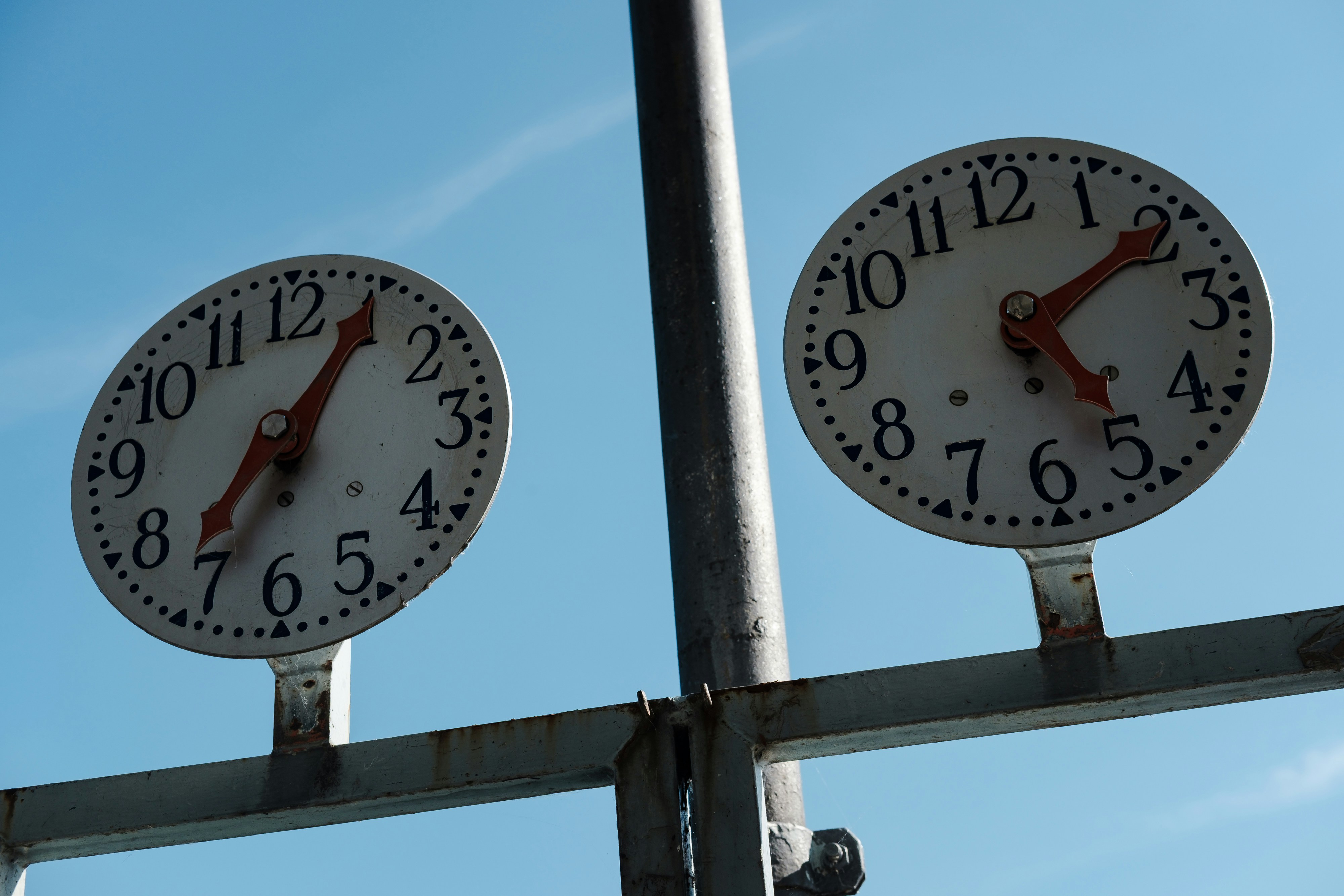 Two clocks show different times against a blue sky.