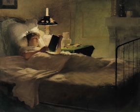 Woman reads book in bed under the lamp.