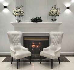 Elegant white chairs face a fireplace adorned with flowers.