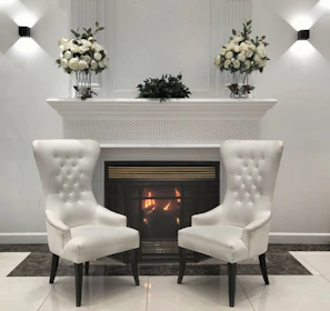 Elegant white chairs face a fireplace adorned with flowers.