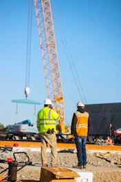 Construction workers observe a crane lifting materials.