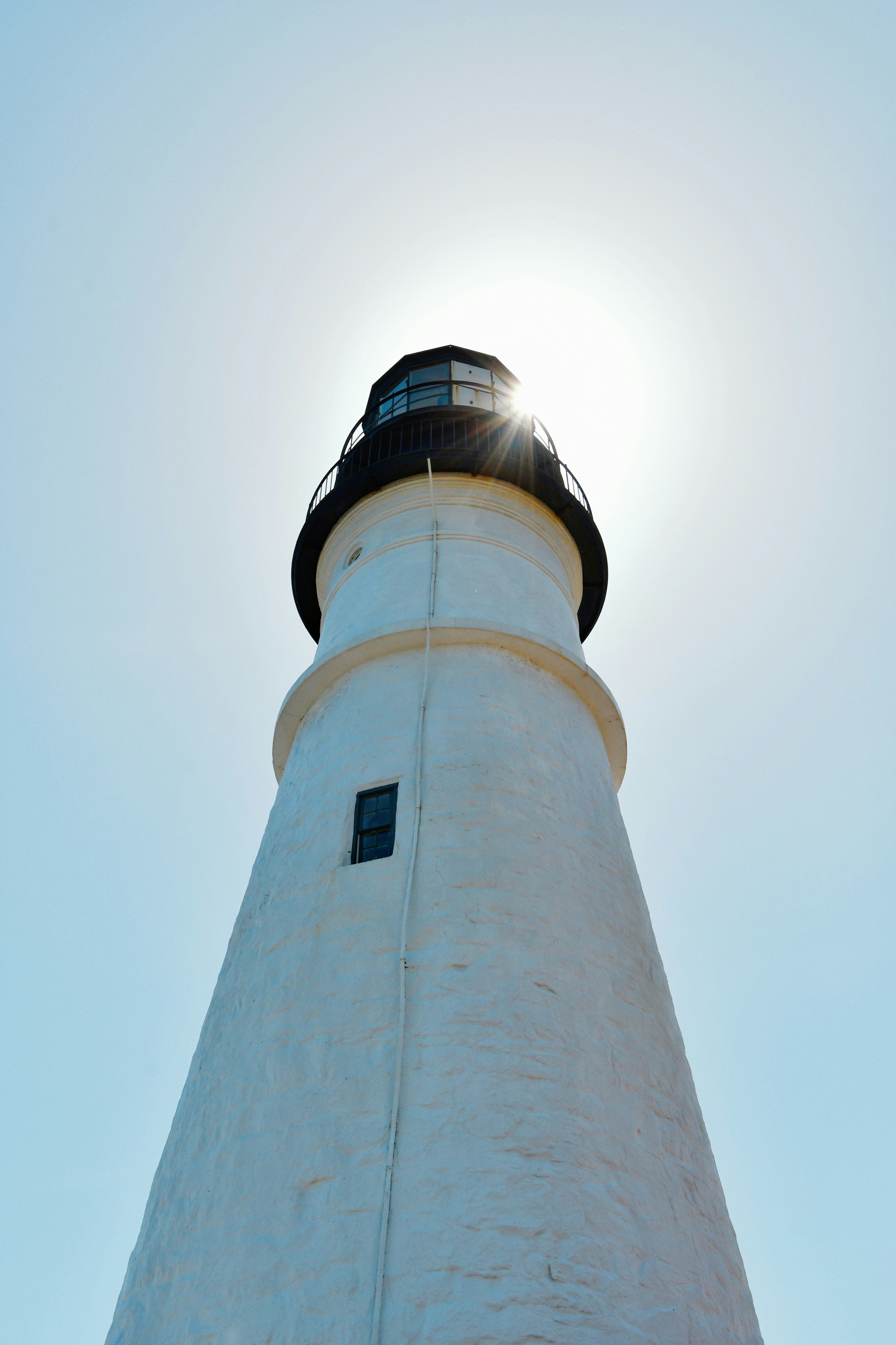 White lighthouse stands tall against the sun.