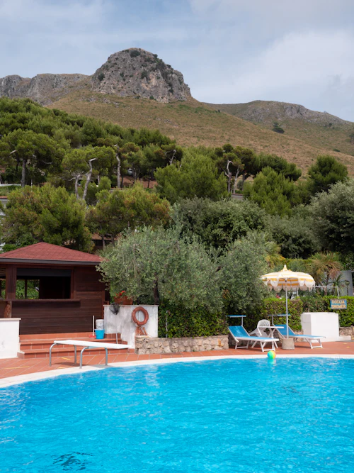 Piscine bleue, transats et parasol devant des oliviers et une colline rocheuse