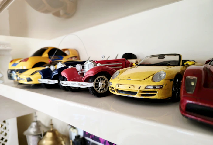 Toy cars are lined up on a white shelf.