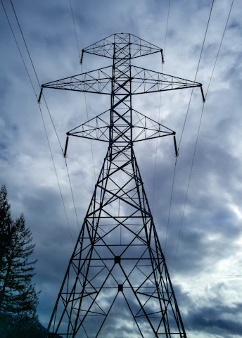 A tall power pylon stands against a cloudy sky.
