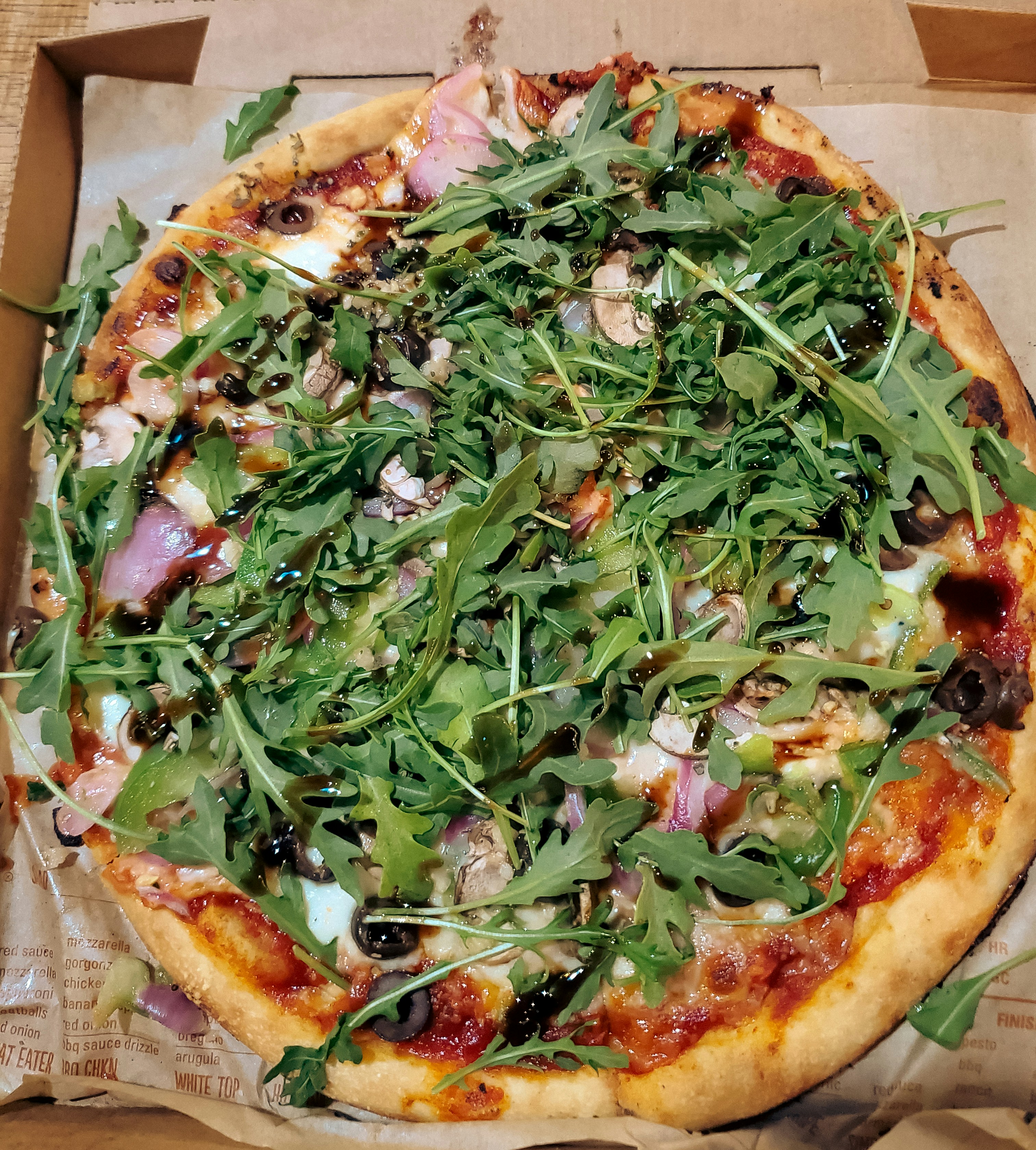 The image shows a freshly baked MOD Pizza served in its signature branded pizza box. The pizza features a thin crust with customizable toppings such as cheese, vegetables, meats, or sauces, depending 