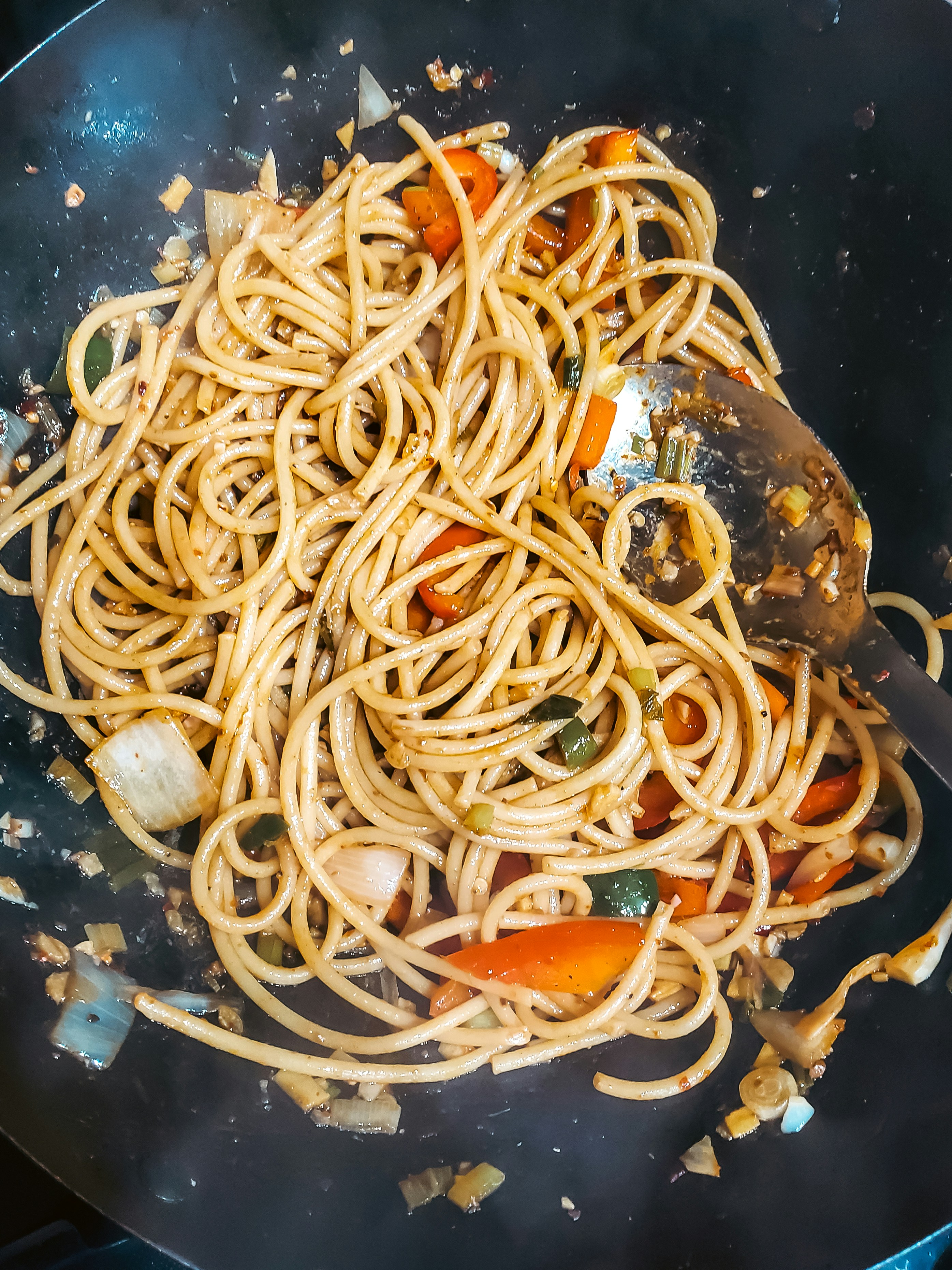 Pasta and vegetables are cooking in a wok.