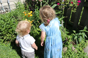 Two young children explore a lush garden.
