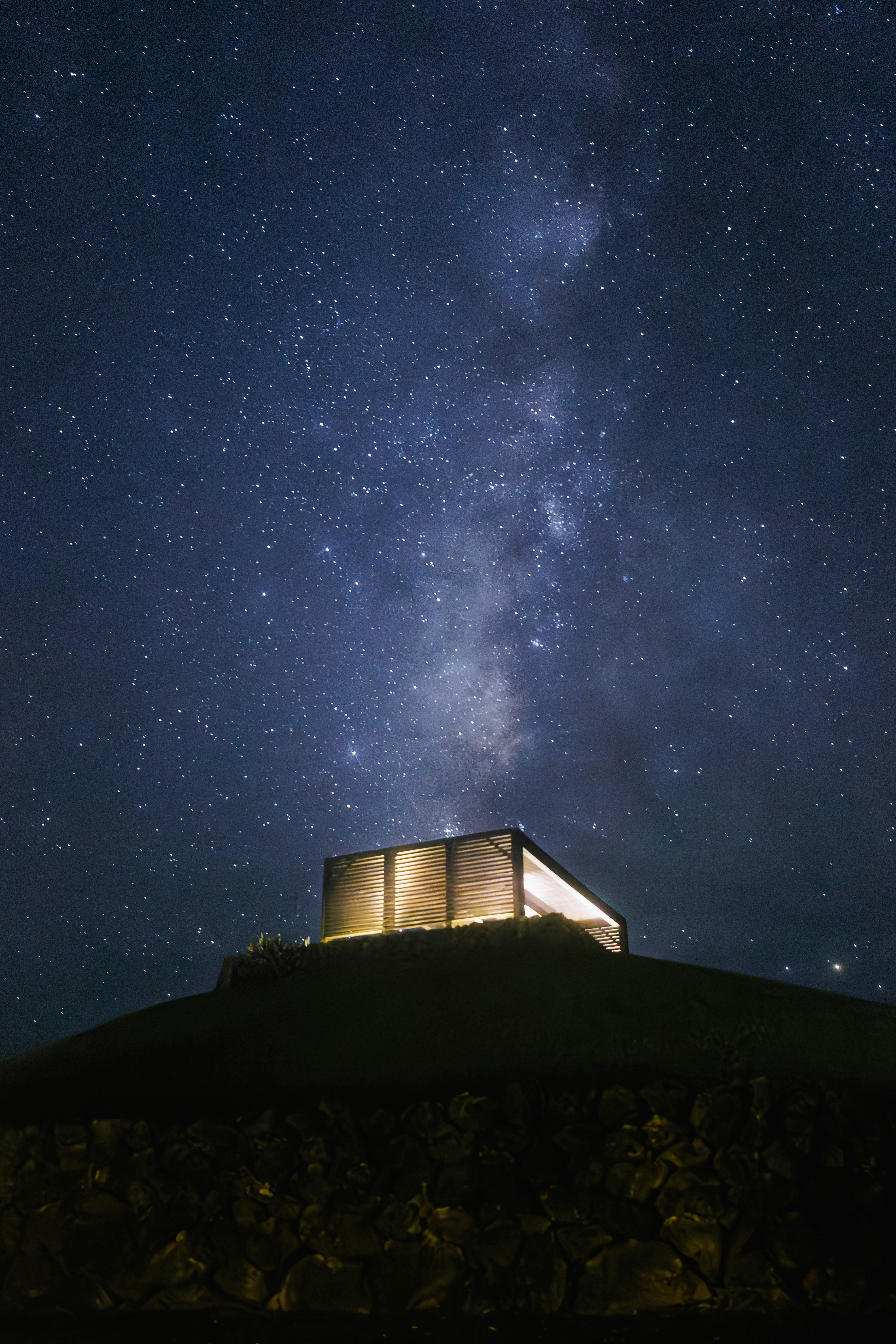 A lit house stands under a starry sky.