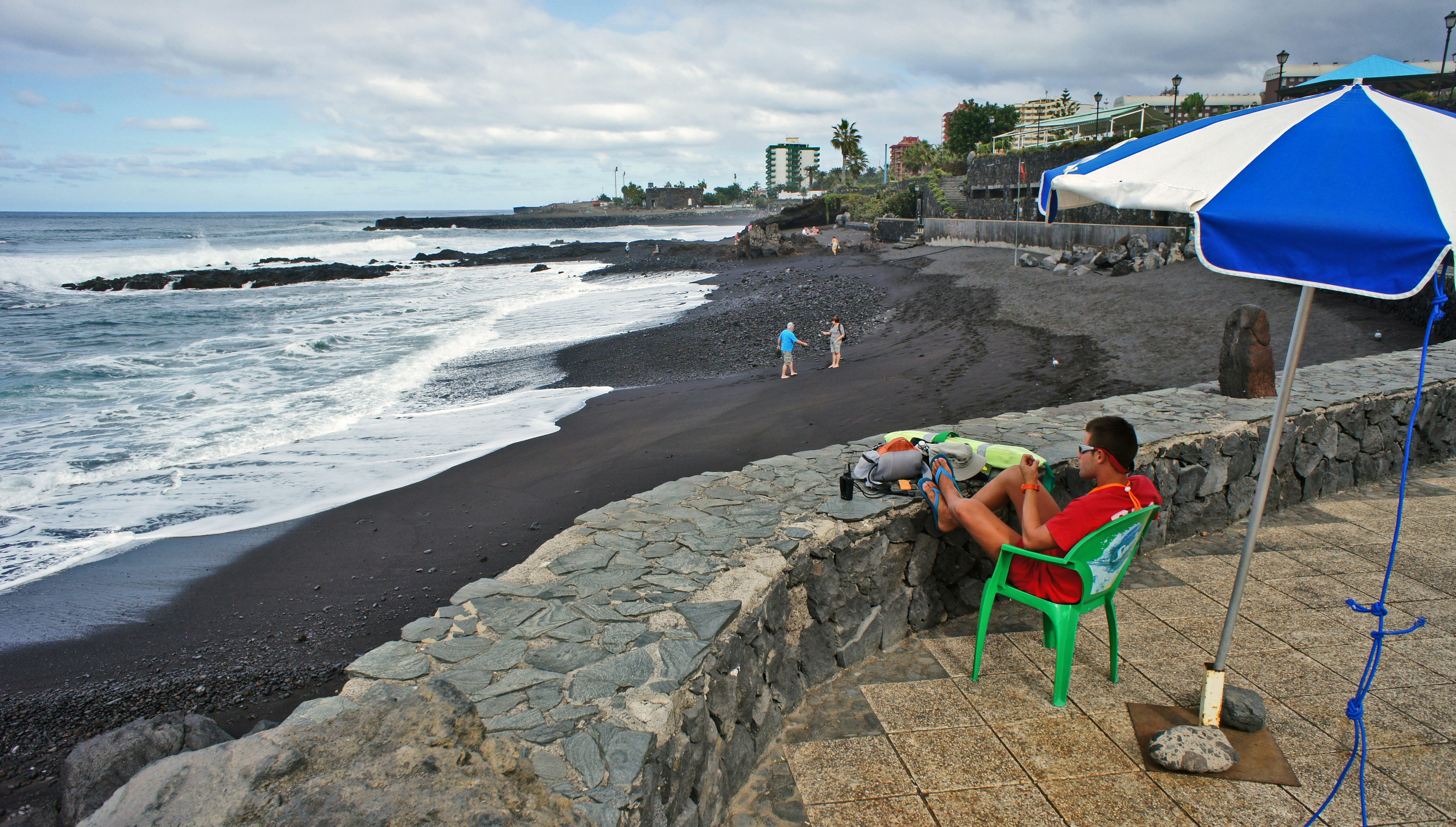 Man relaxes by a black sand beach.