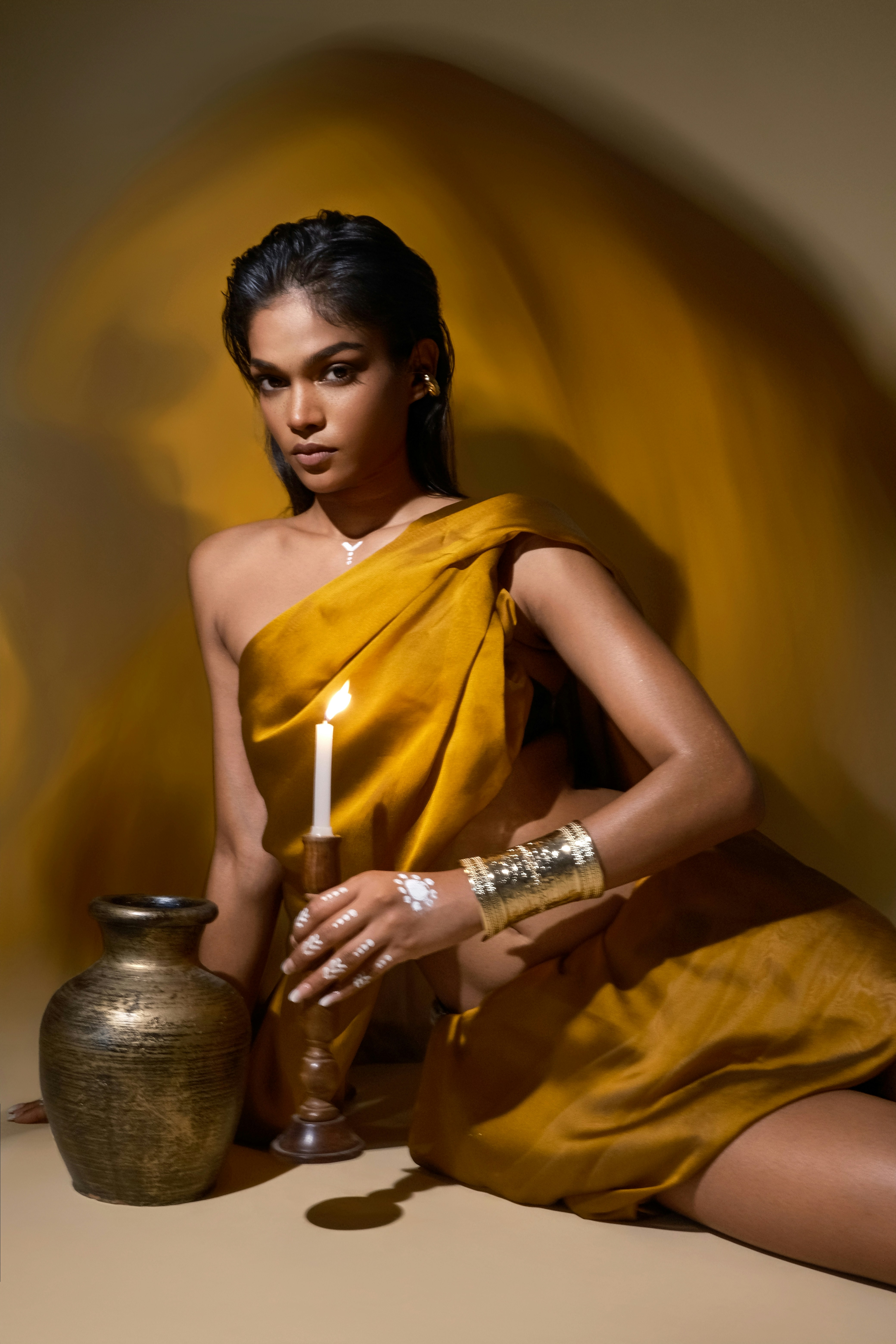 Woman in yellow holding a candle and looking at the camera.