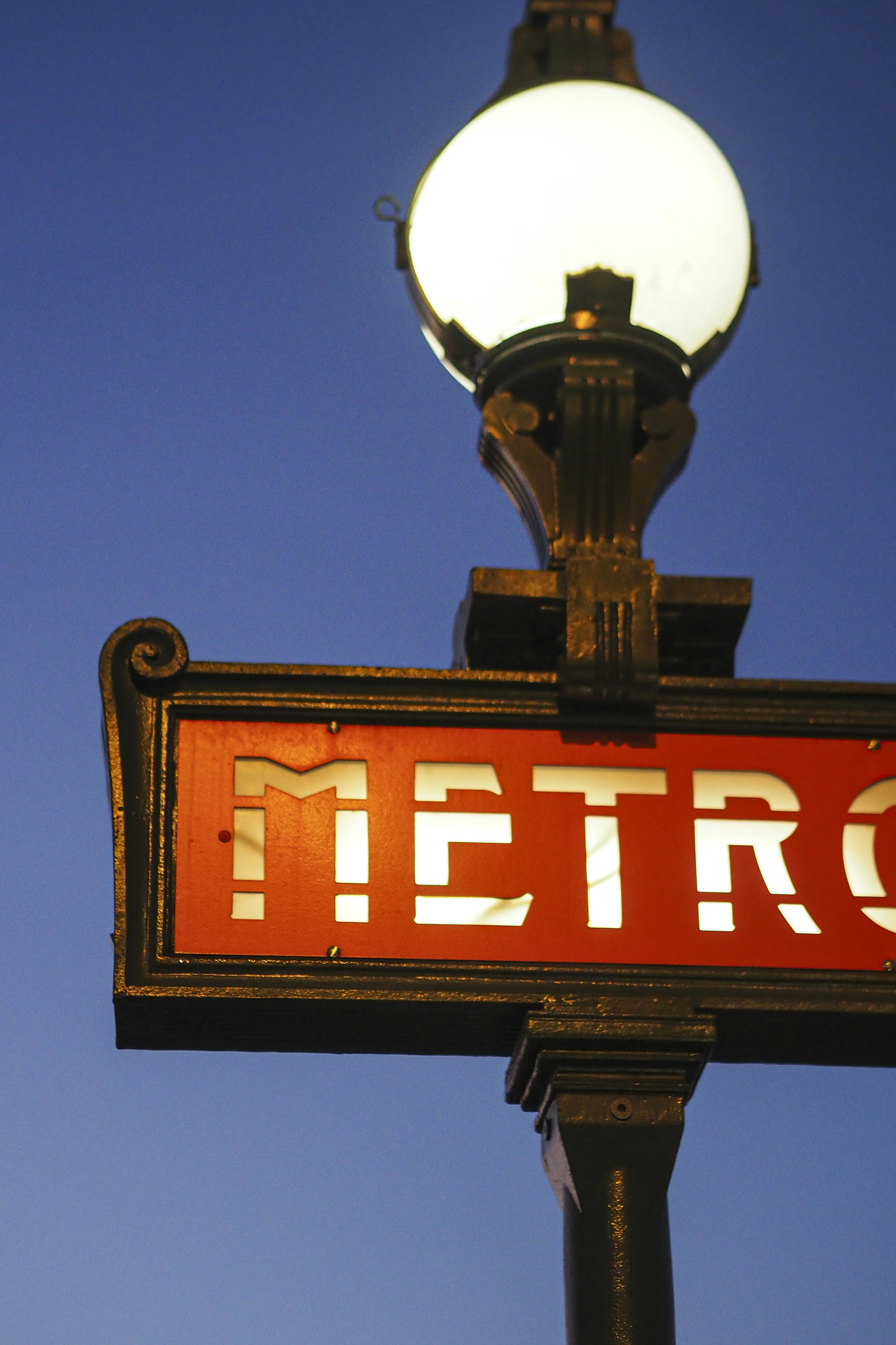 A paris metro sign glows brightly at dusk.