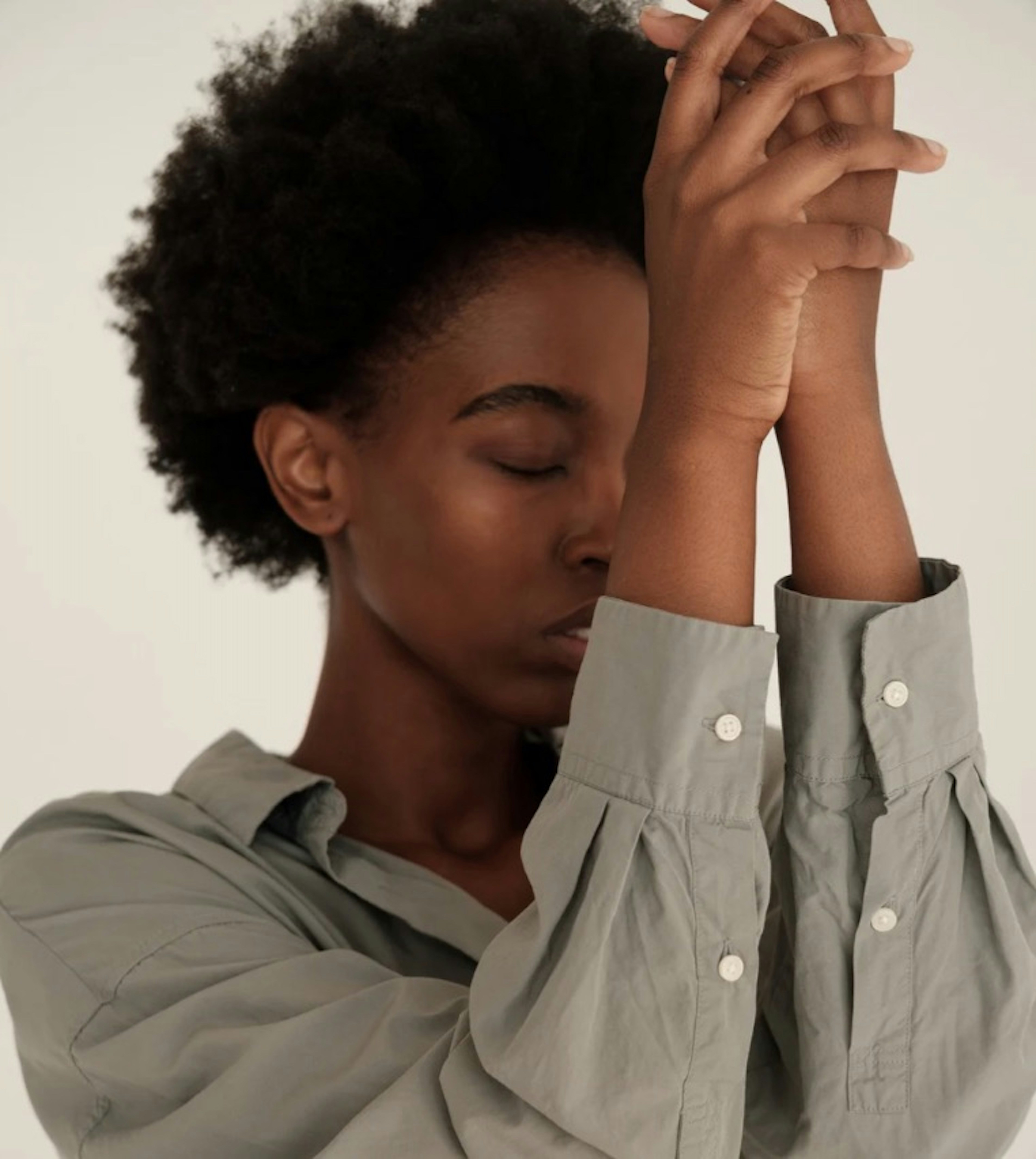 Woman closes eyes with hands clasped together.