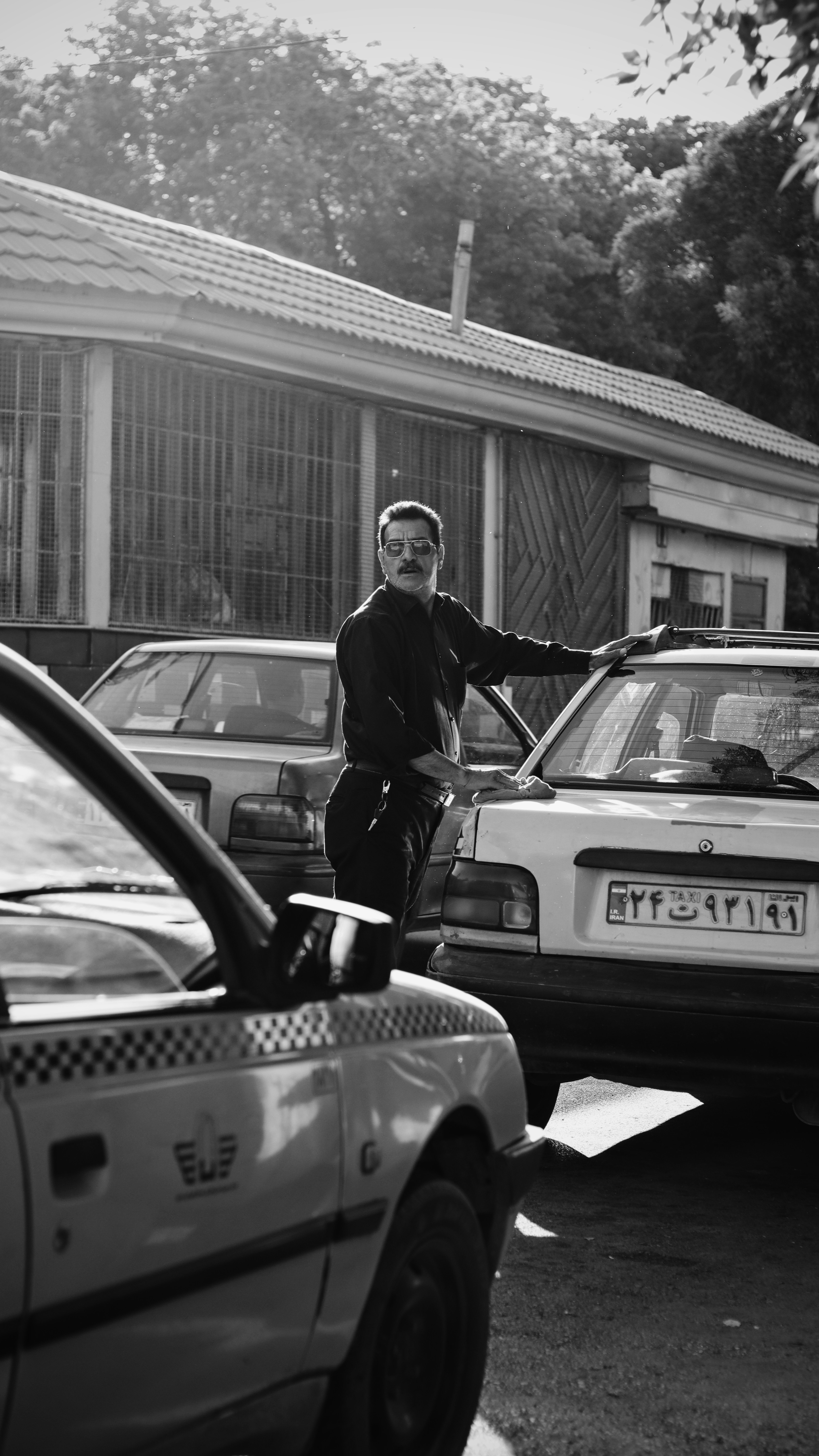 A man stands next to cars in black and white.