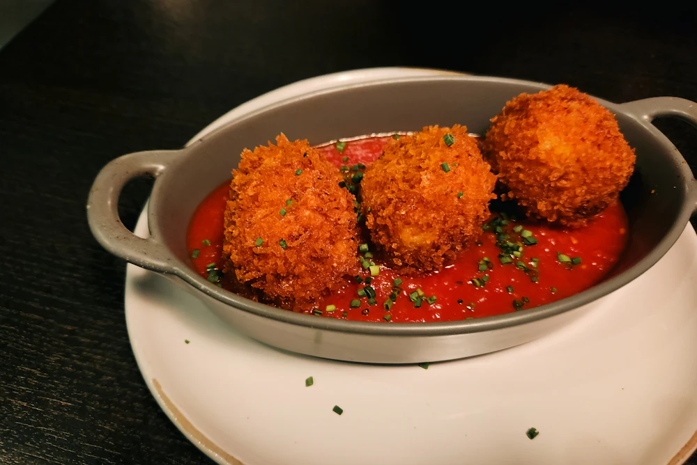 Supplì fritti dorati serviti in un tegamino con salsa di pomodoro