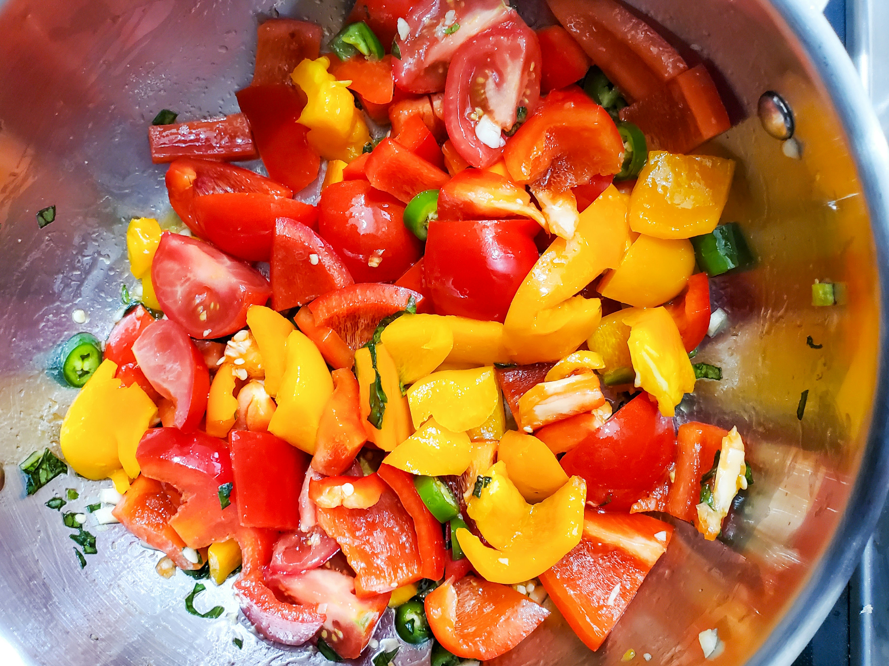 Chopped vegetables are mixed in a stainless steel bowl.