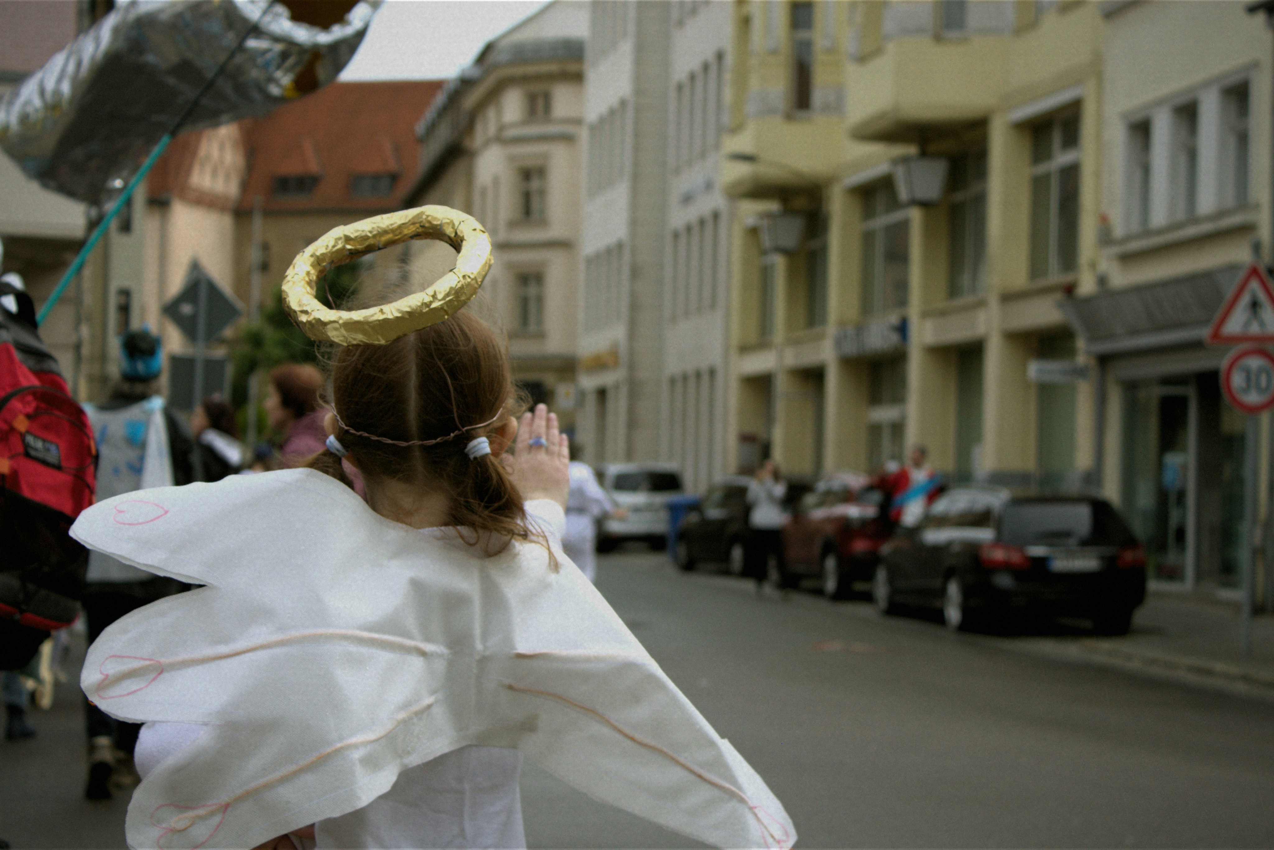 A child in angel costume walks down the street.