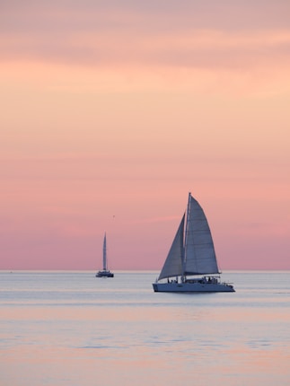 Sailboats glide peacefully under a pastel sunset.