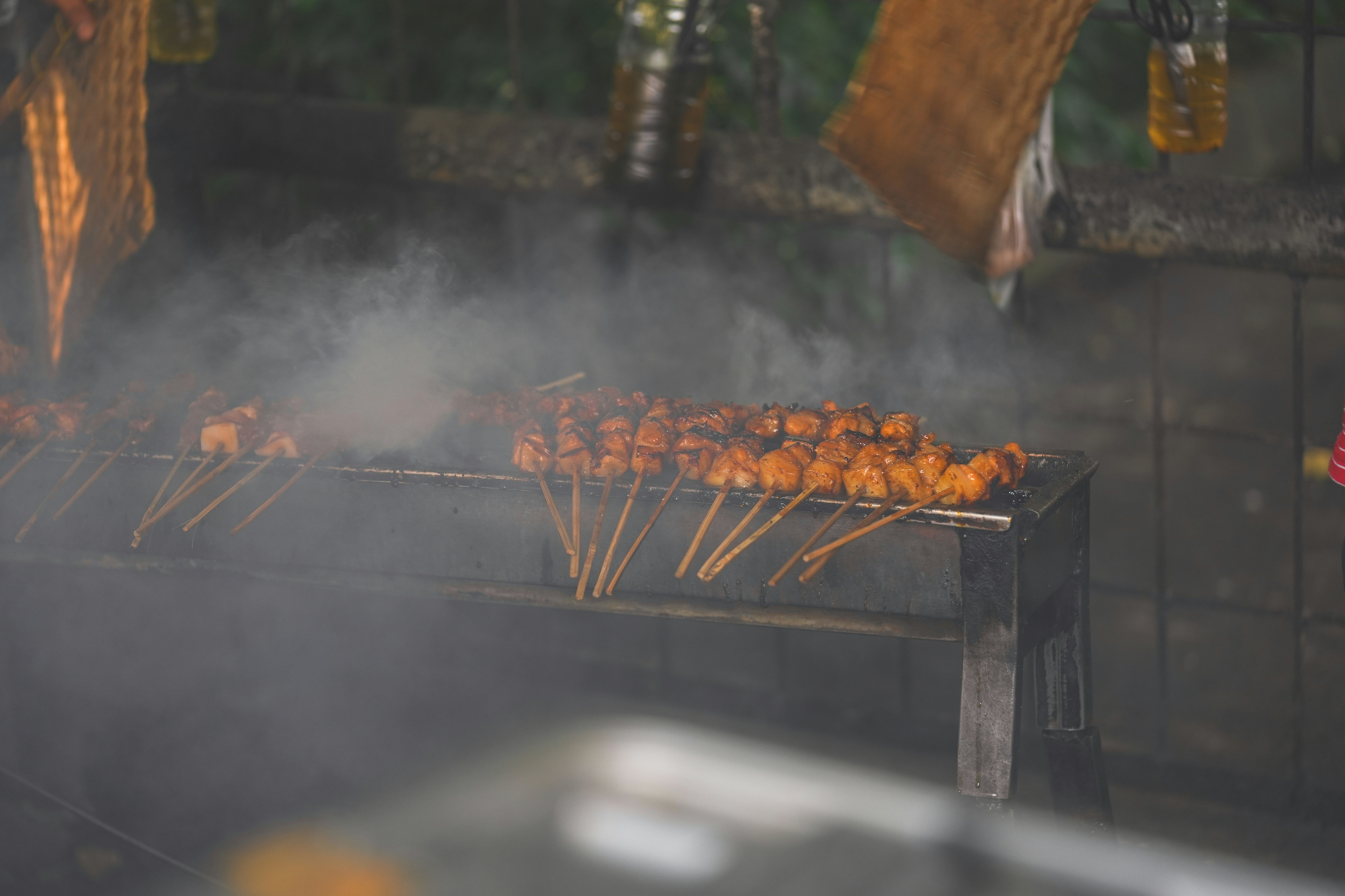 Skewered meat cooks over a grill, creating smoke.