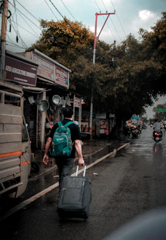 Man walks down a wet street, pulling a suitcase.