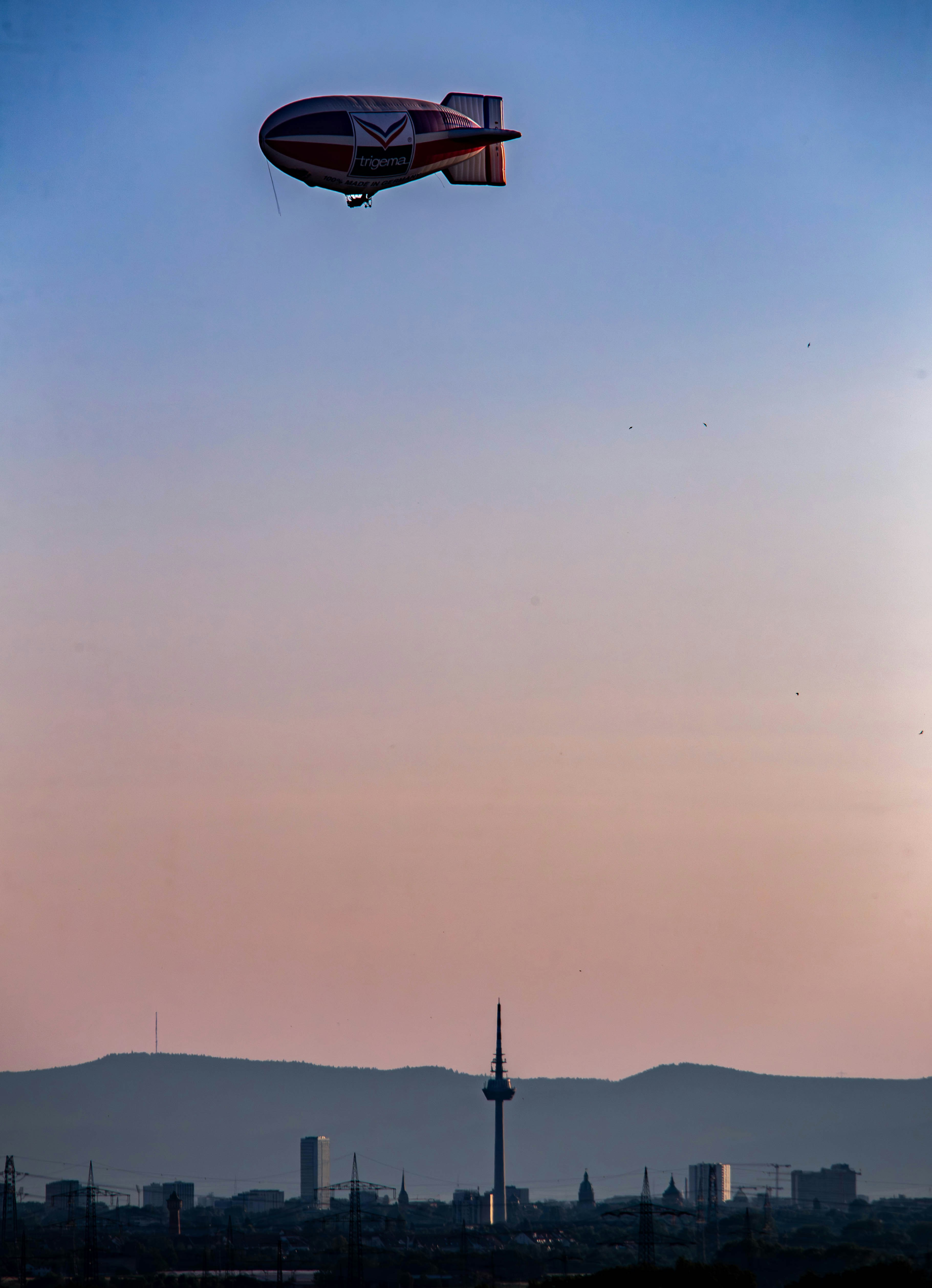 Airship flying over a city during sunset.