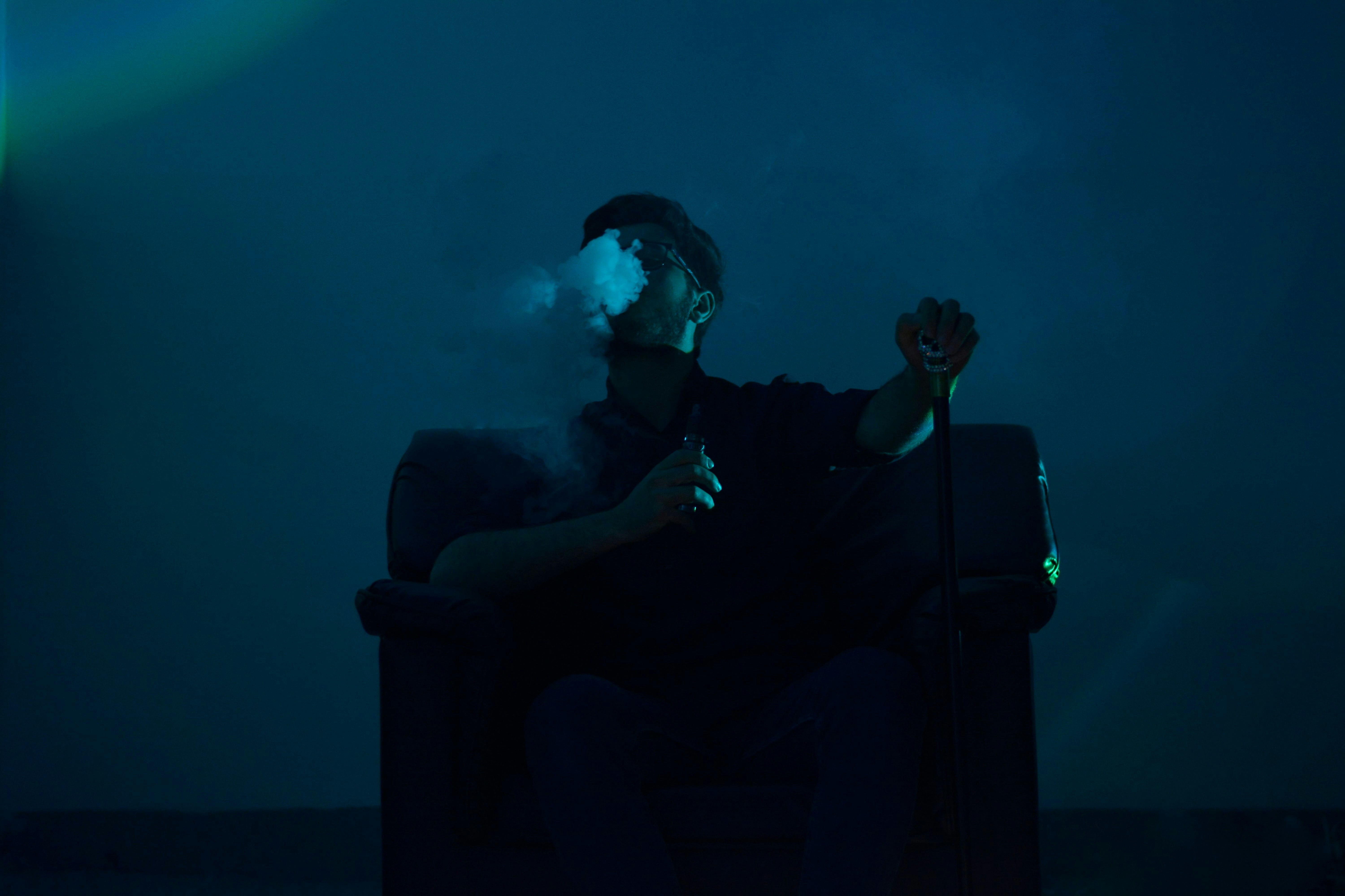 Man exhales vape smoke in a dimly lit room.