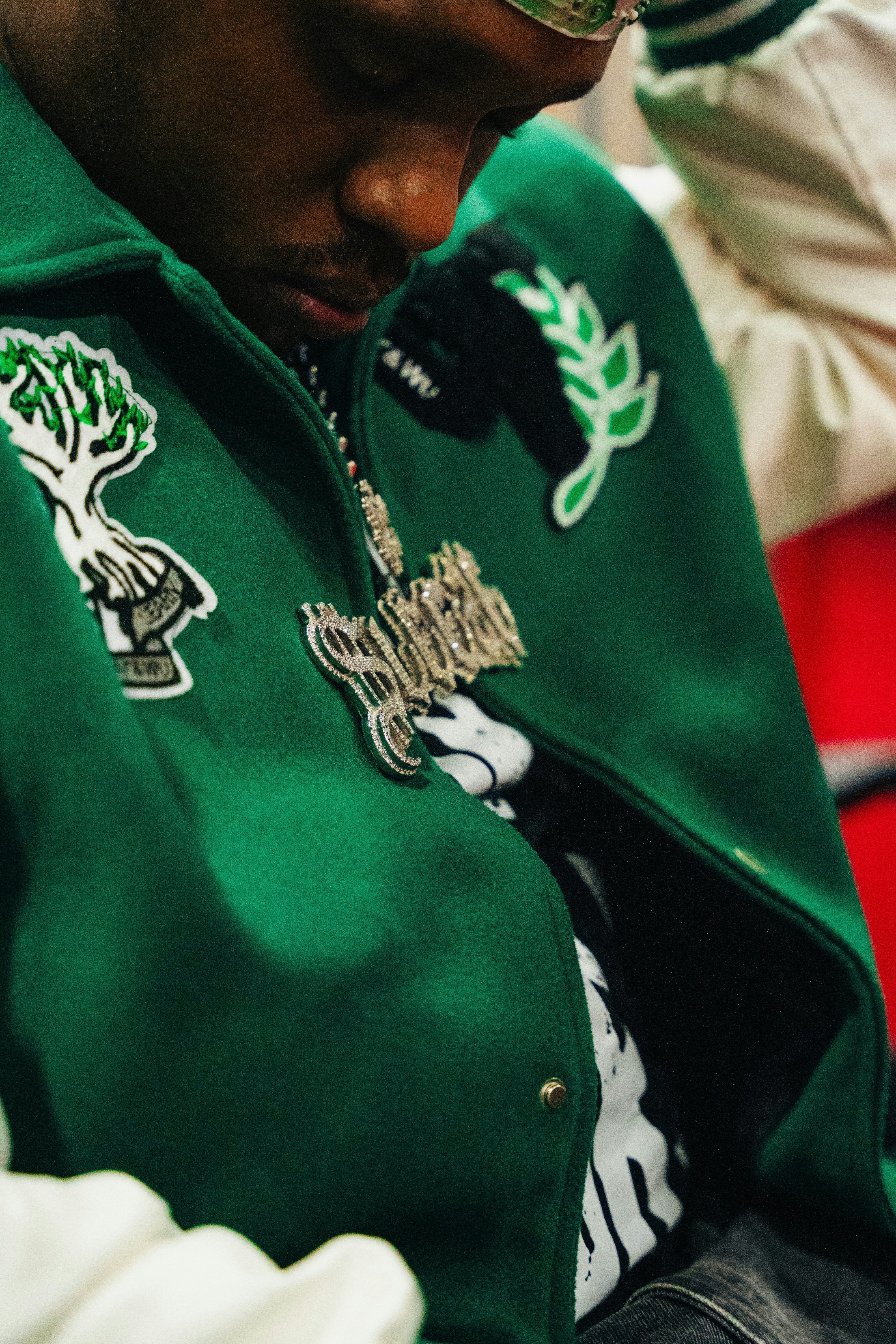 A person wearing a green jacket and a necklace.