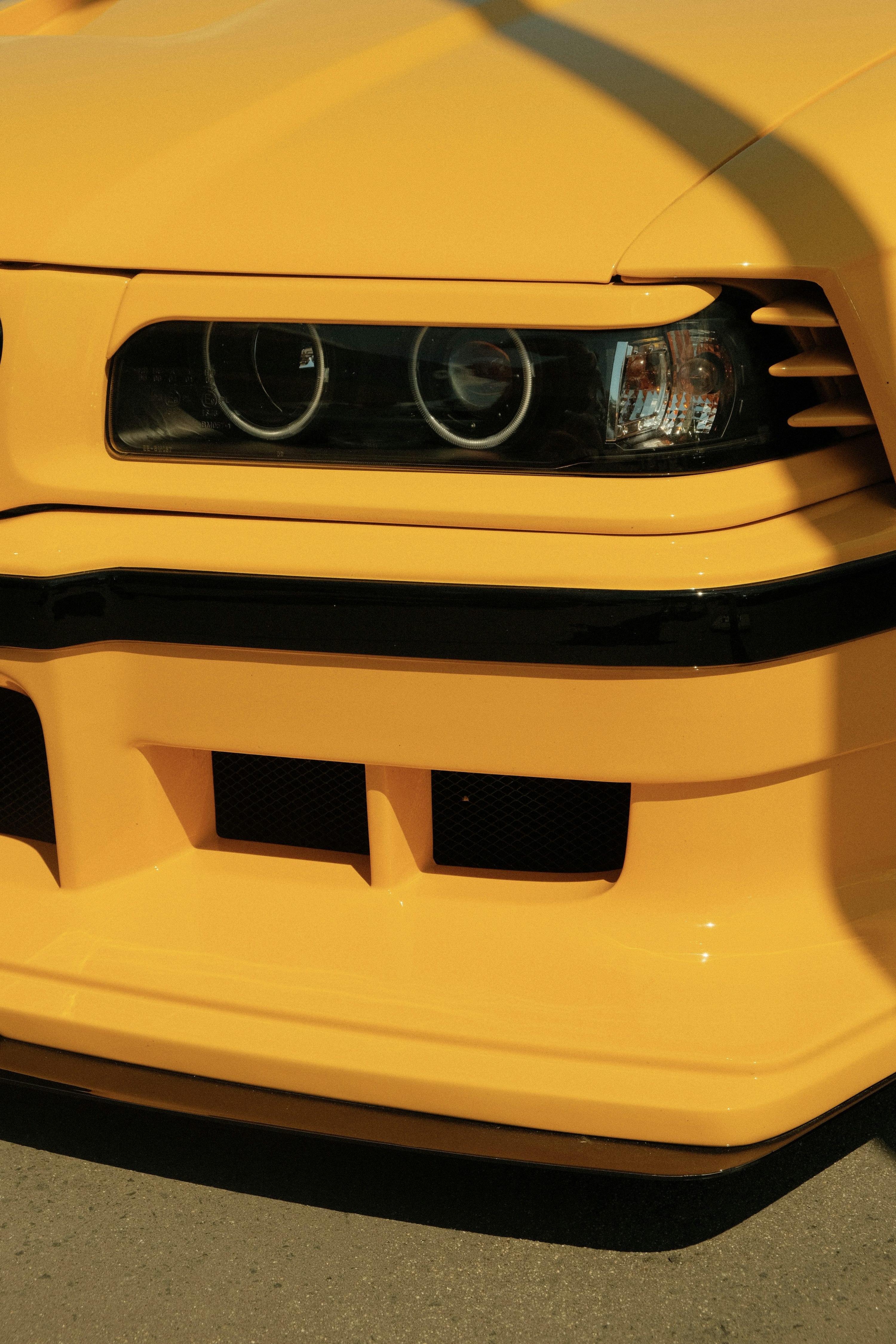 Yellow bmw's front, showing its headlight and bumper.