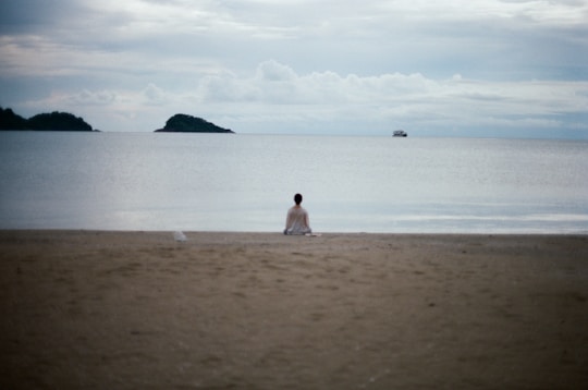 Person meditating on a quiet beach facing the ocean.