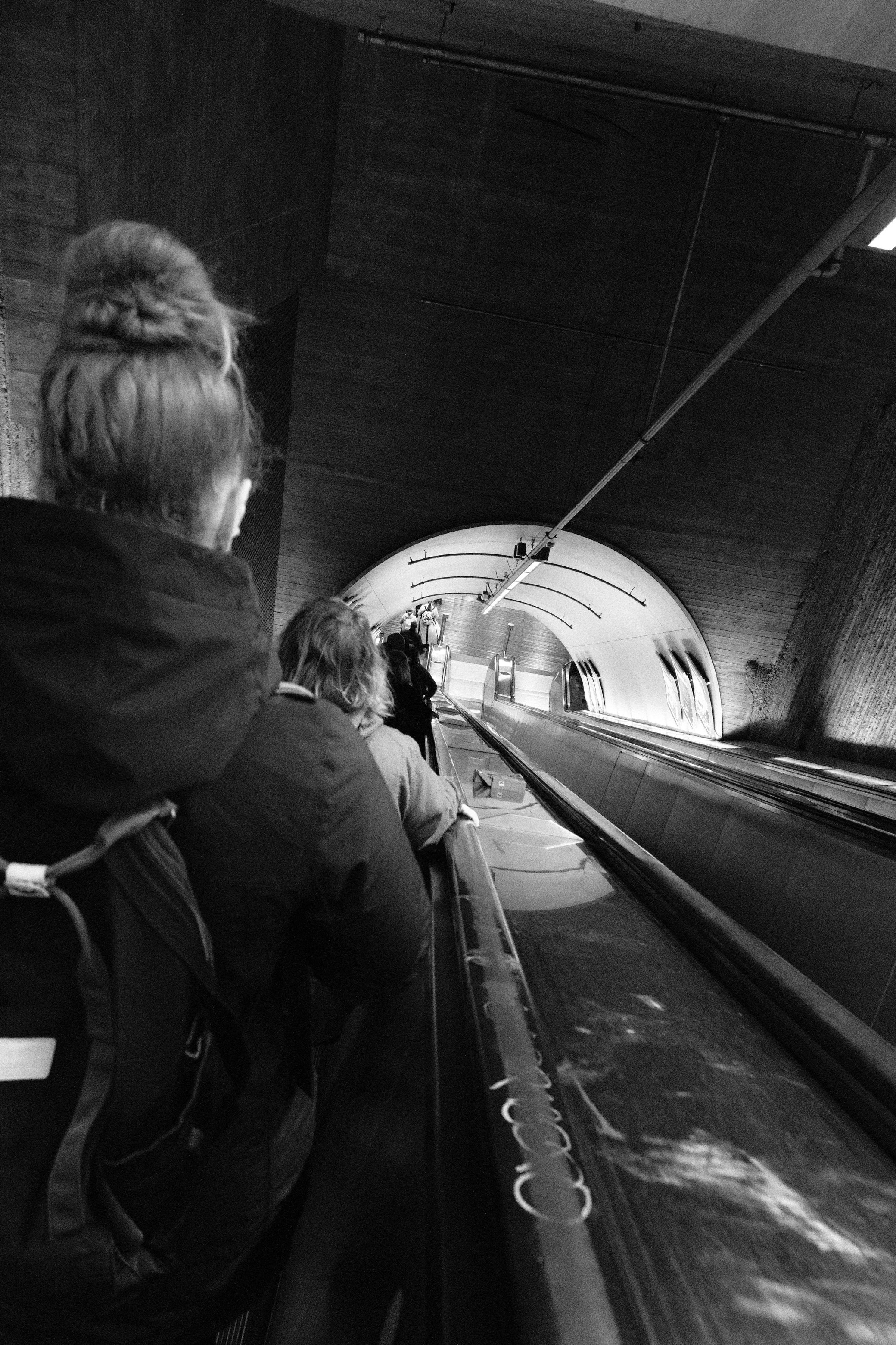People ride an escalator into a long, dark tunnel.