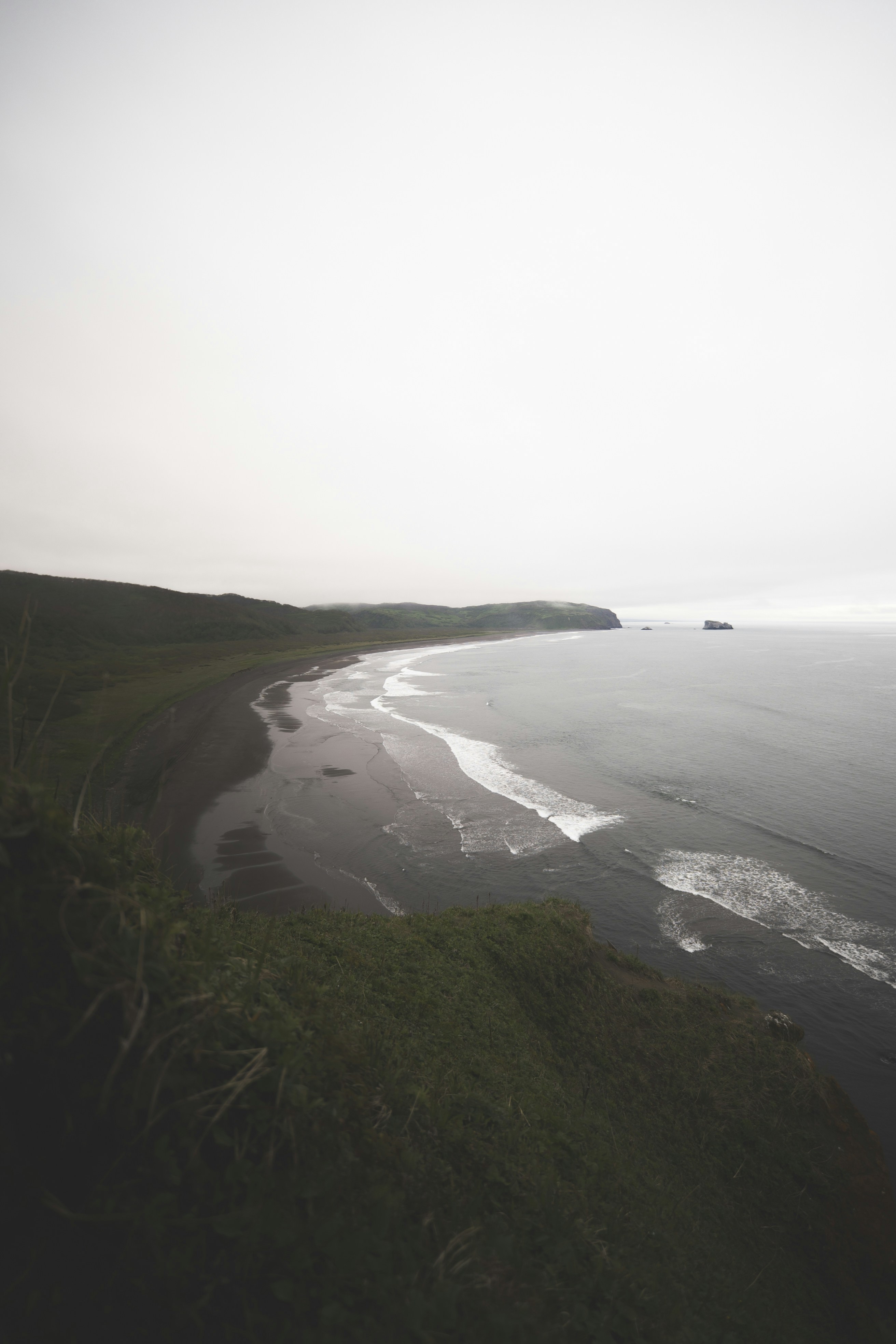 A beach is curved, with waves and a cloudy sky.
