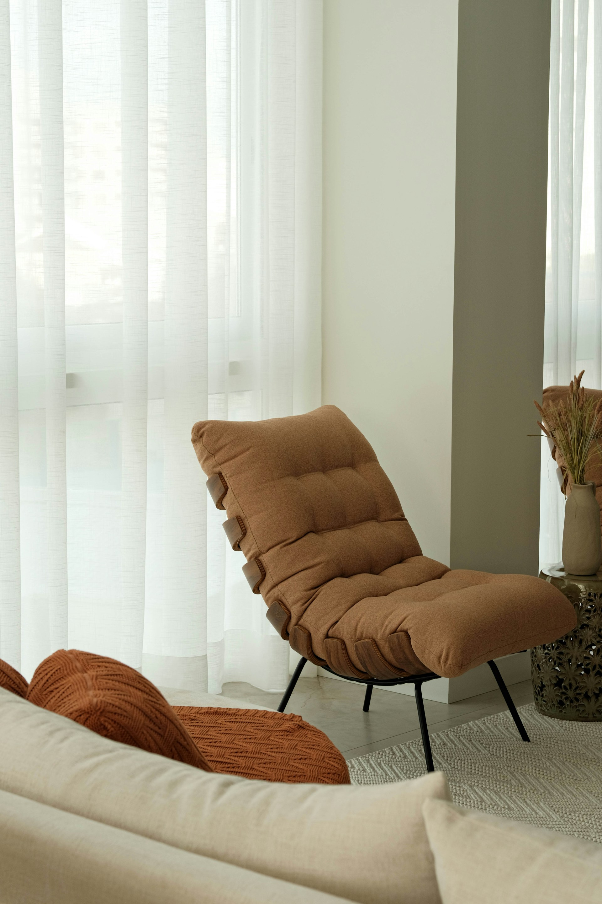 A cozy, modern chair sits near a sheer curtain.