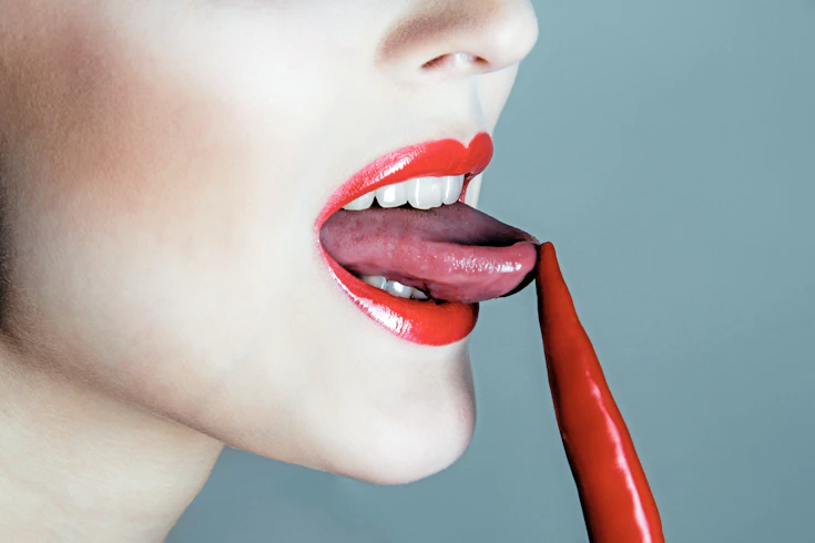 Woman licking a red chili pepper.
