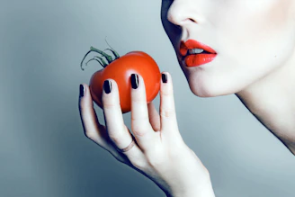 Woman holds a tomato, ready to eat.