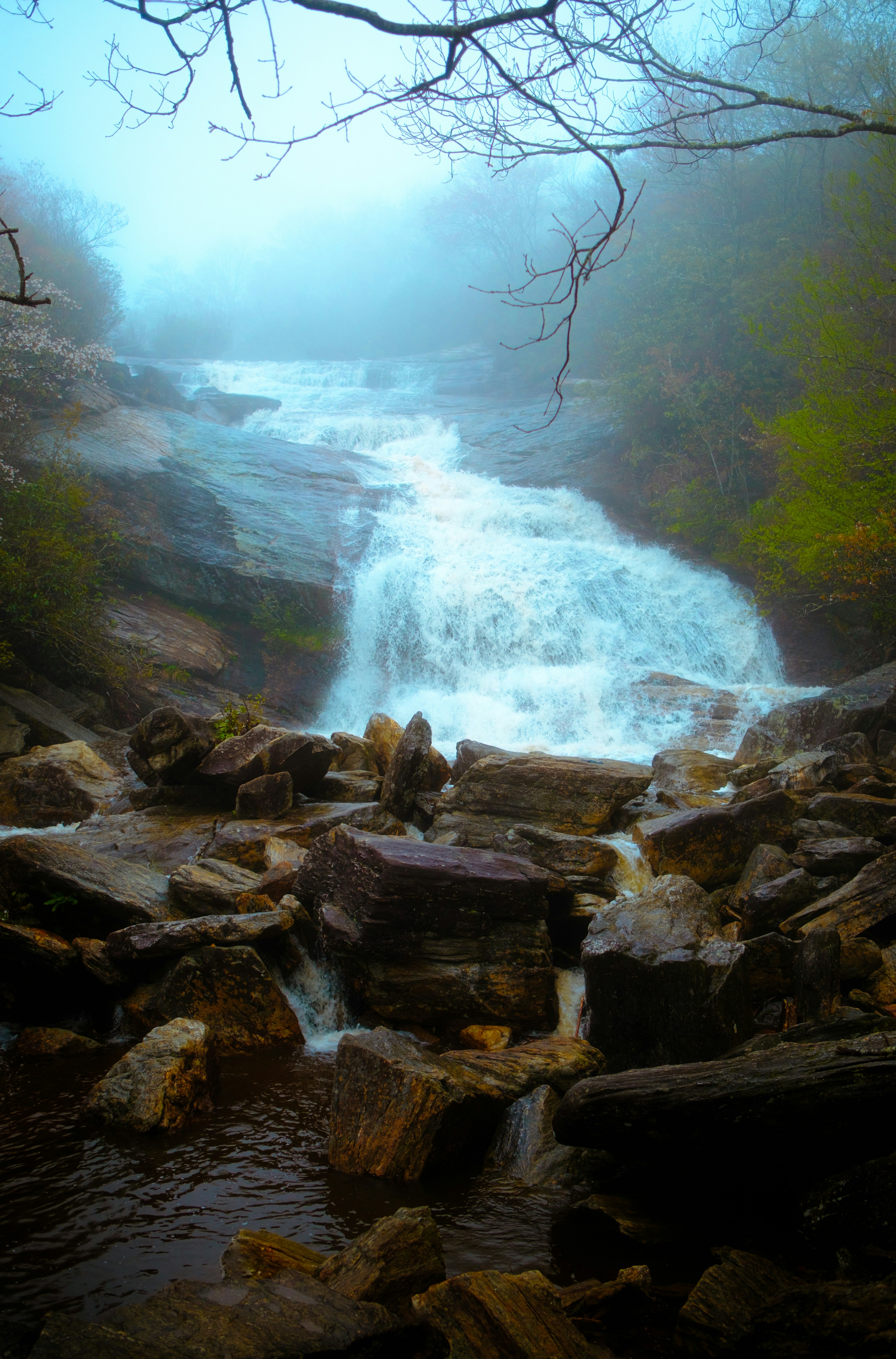 A waterfall cascades through foggy mountains.