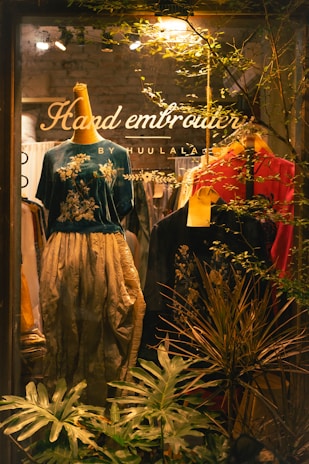 Shop window displays embroidered clothing and greenery.