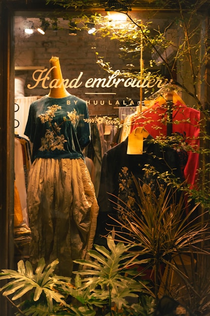 Shop window displays embroidered clothing and greenery.