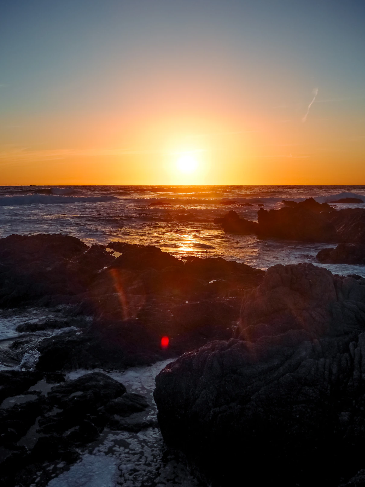 Sunset over the ocean with rocks in the foreground.