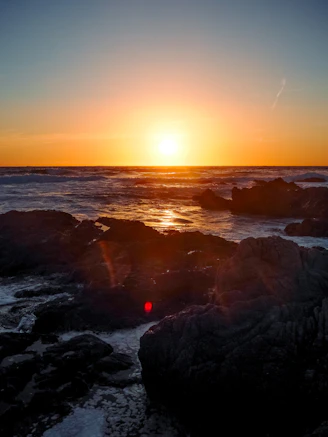 Sunset over the ocean with rocks in the foreground.