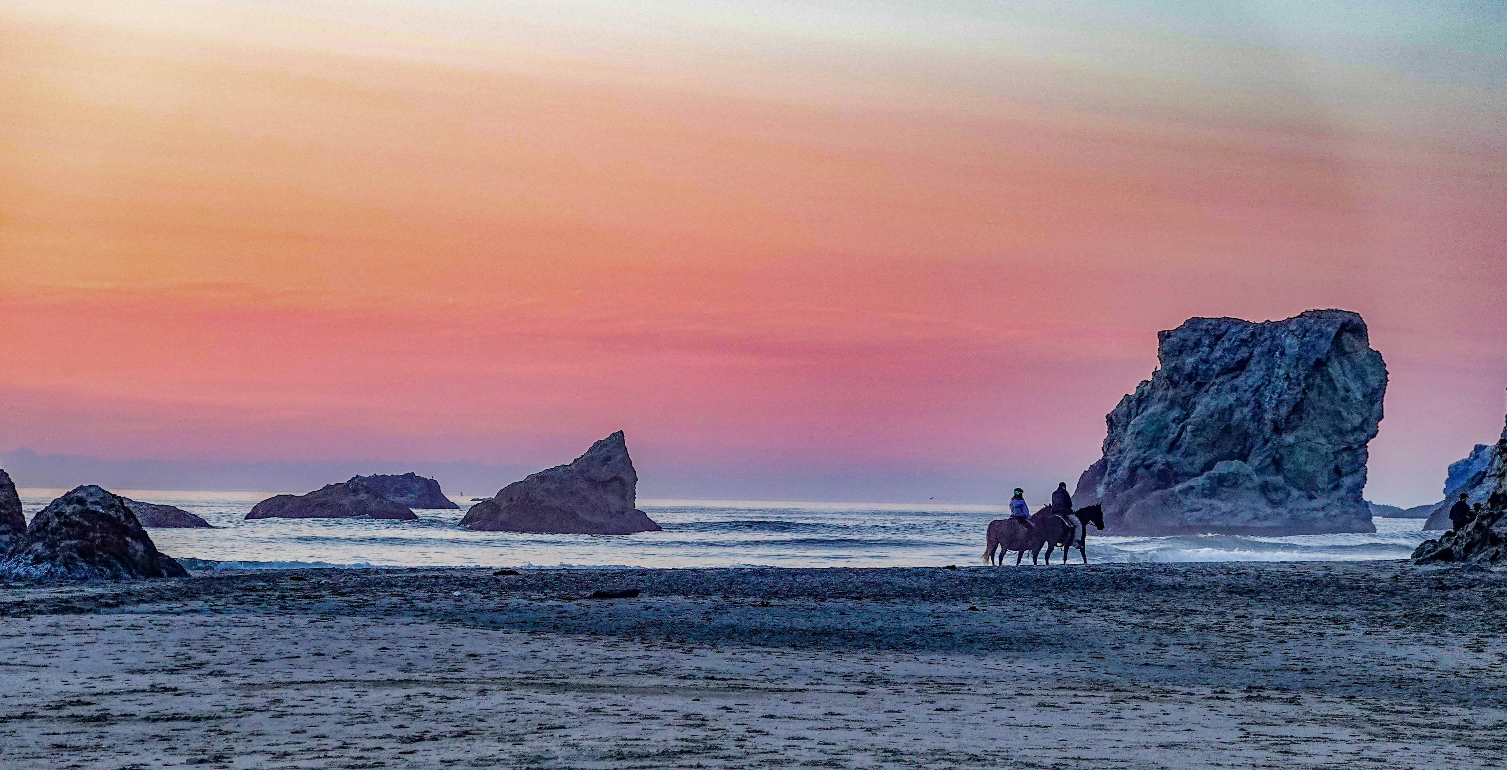 Sunset scene with horses riding on the beach.
