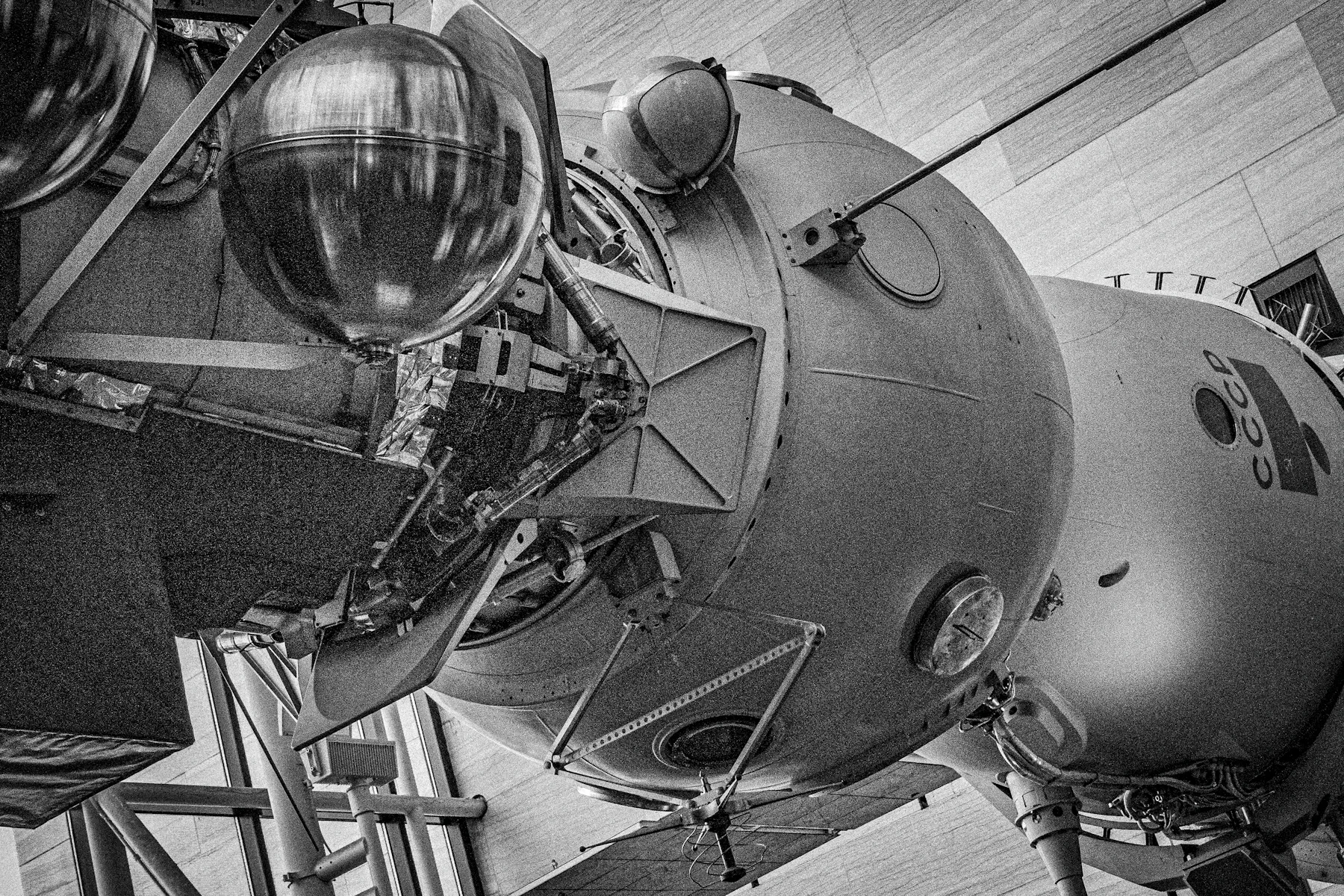 Black and white view of a Soviet spacecraft with spherical tanks and a docking probe on display in a museum