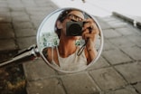 A woman takes a photo in a motorcycle mirror.