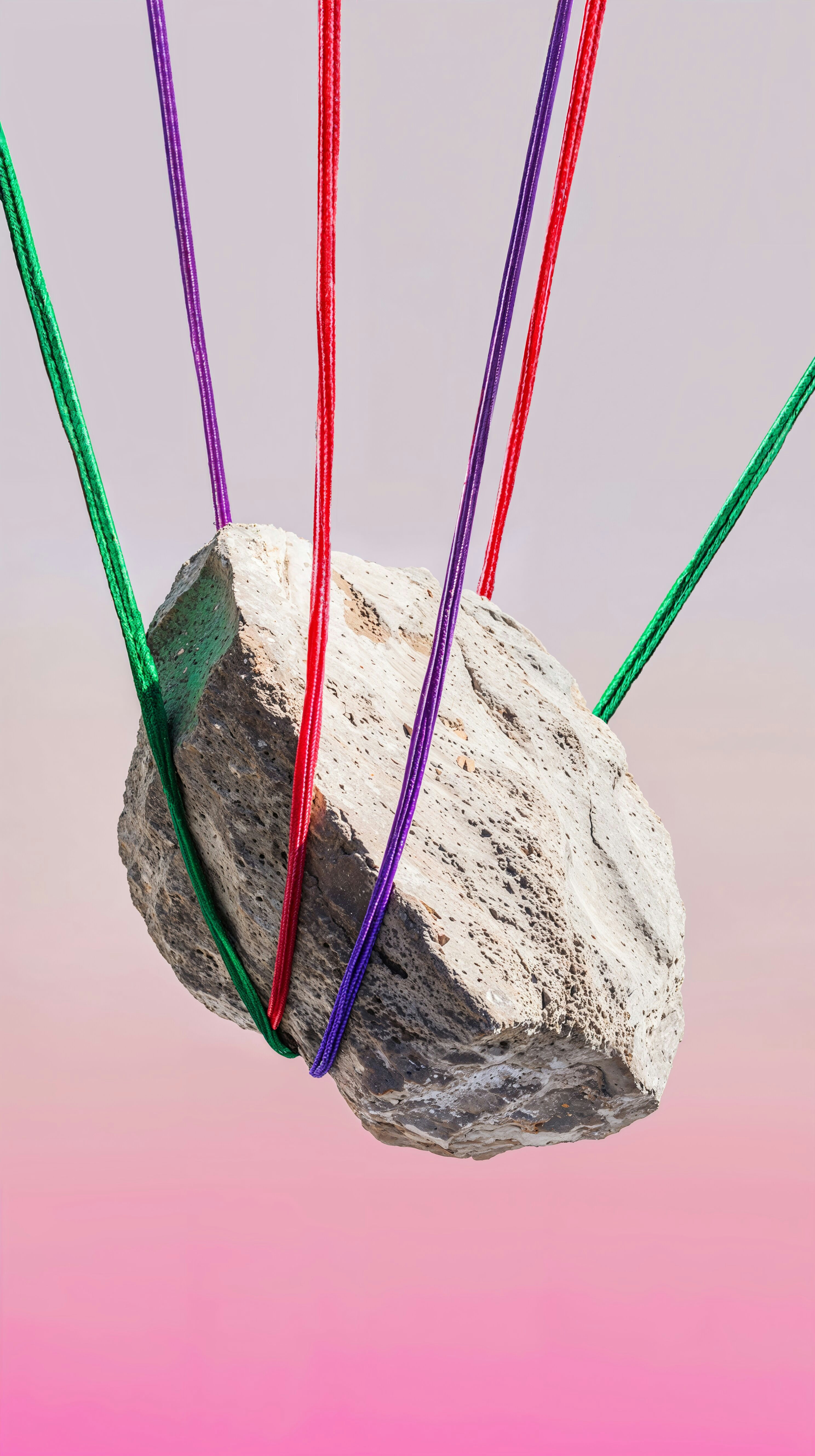 A stone is suspended by colorful ropes.