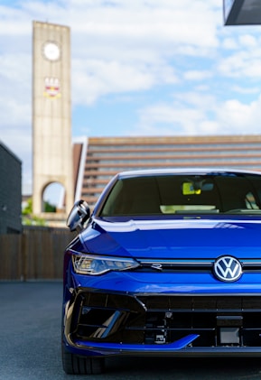 A blue volkswagen golf r stands near a clock tower.