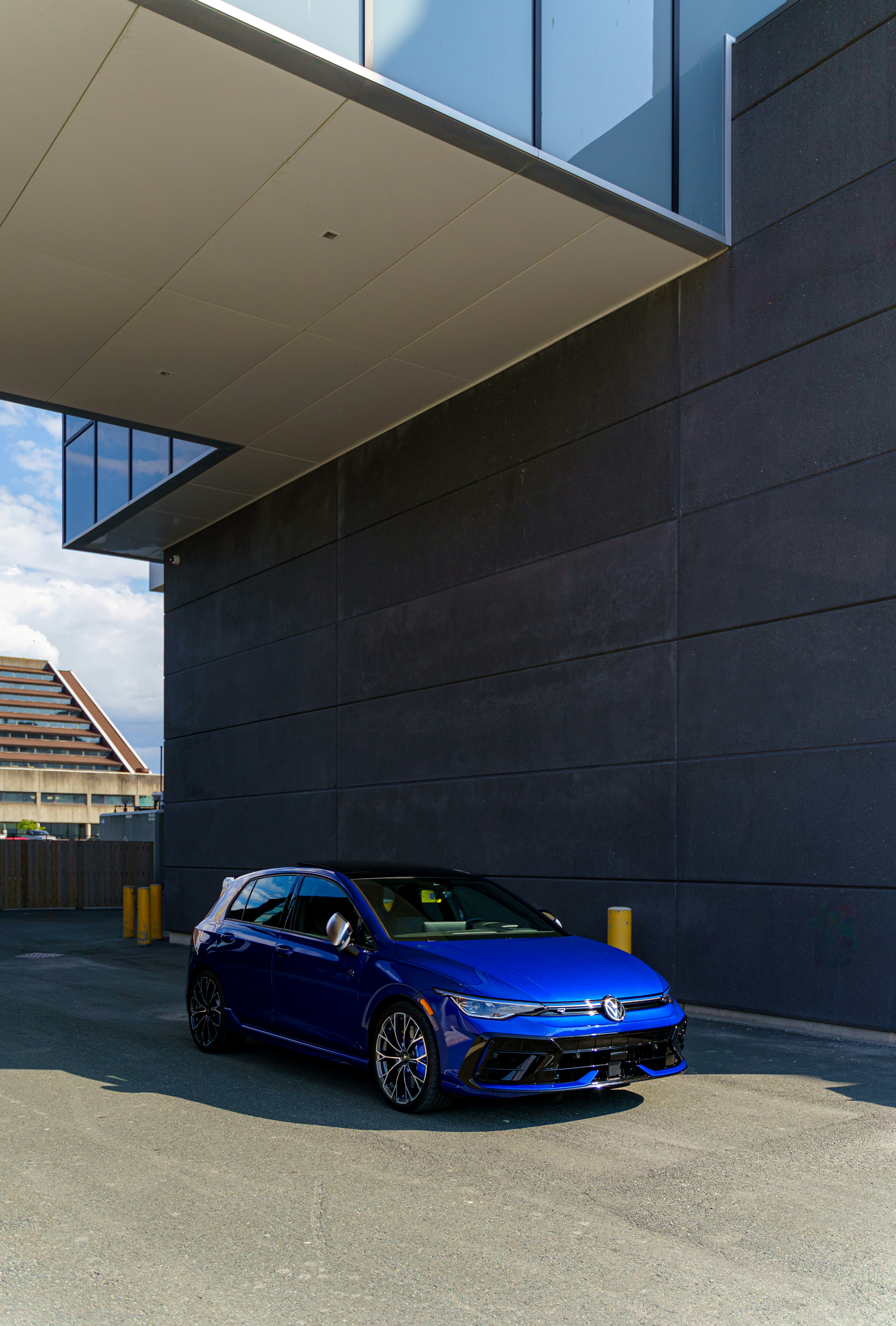 A blue car parks underneath a modern building