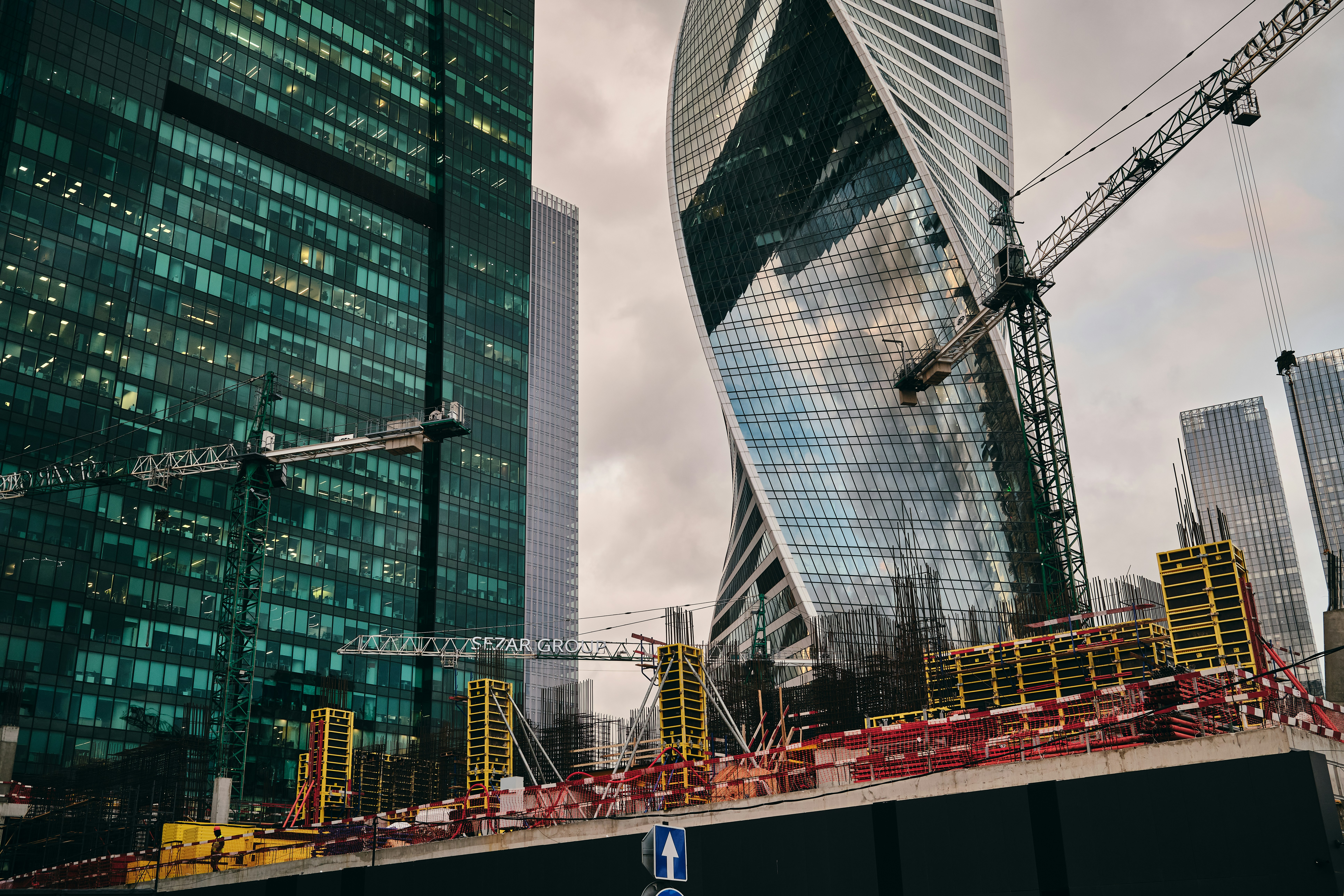 Construction cranes and skyscrapers against cloudy skies.