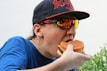 Man wearing sunglasses and a hat is eating a burger.