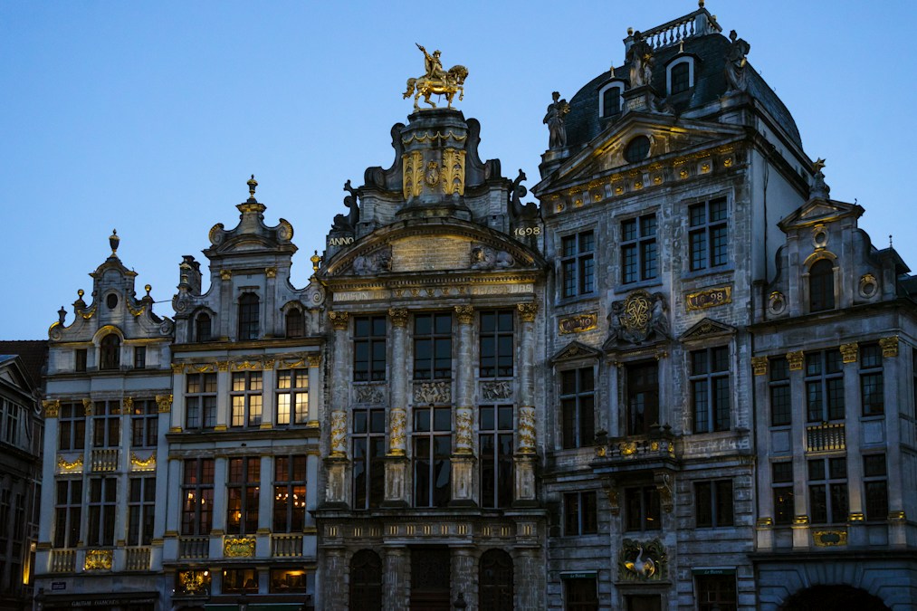 Les façades ornées de la Grand-Place de Bruxelles s’illuminent à la tombée de la nuit, sous un ciel bleu