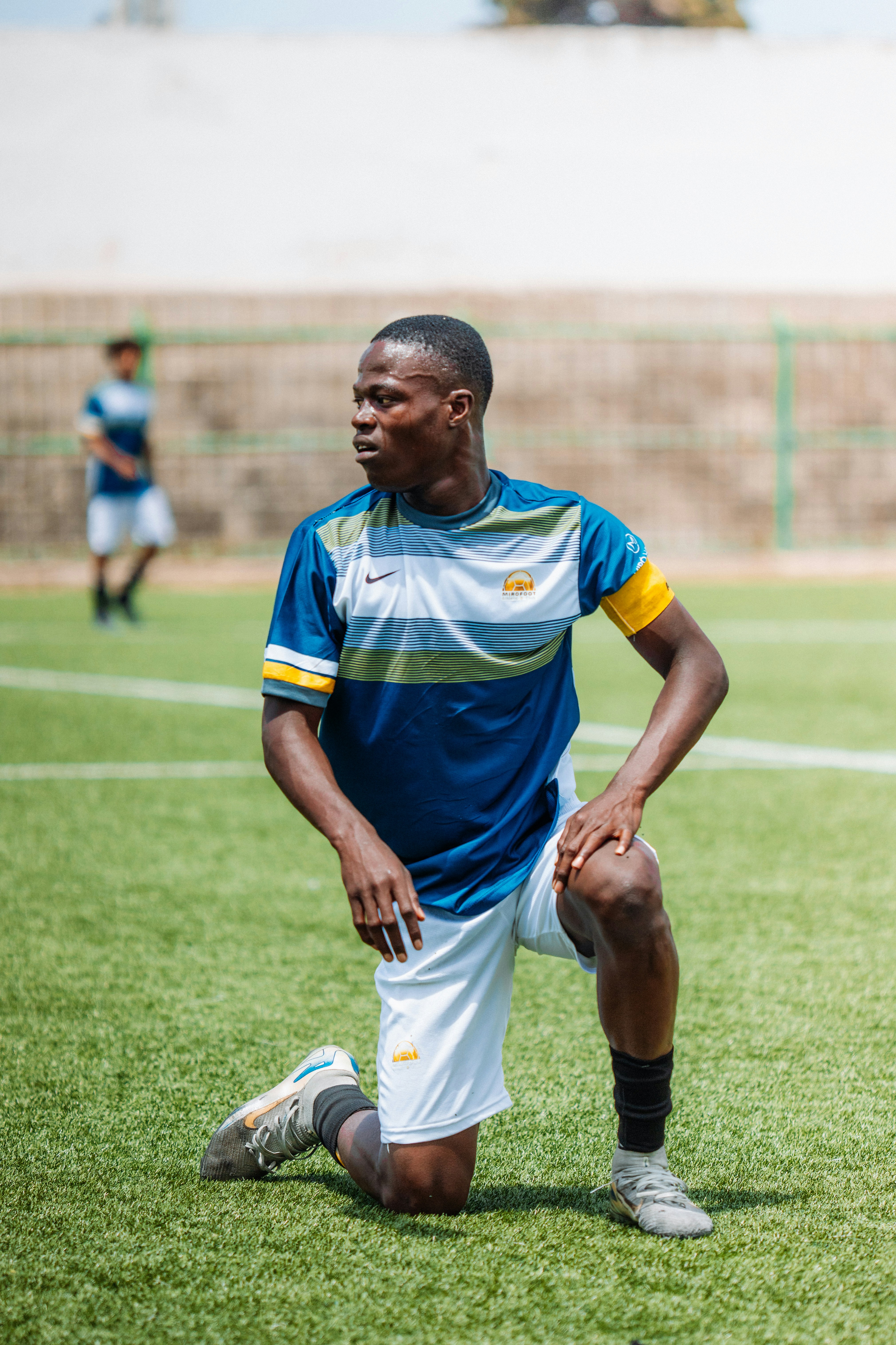 Soccer player is kneeling on the field looking away.